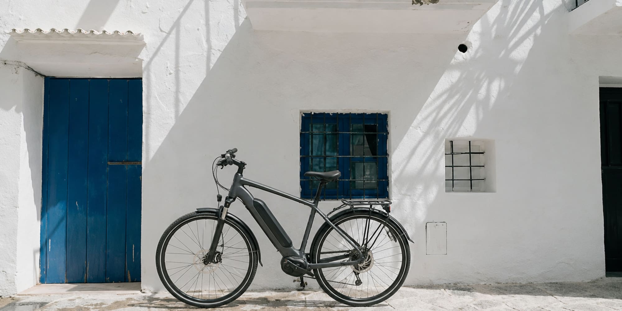 Modern e-bike parked against a white Mediterranean building with blue door.