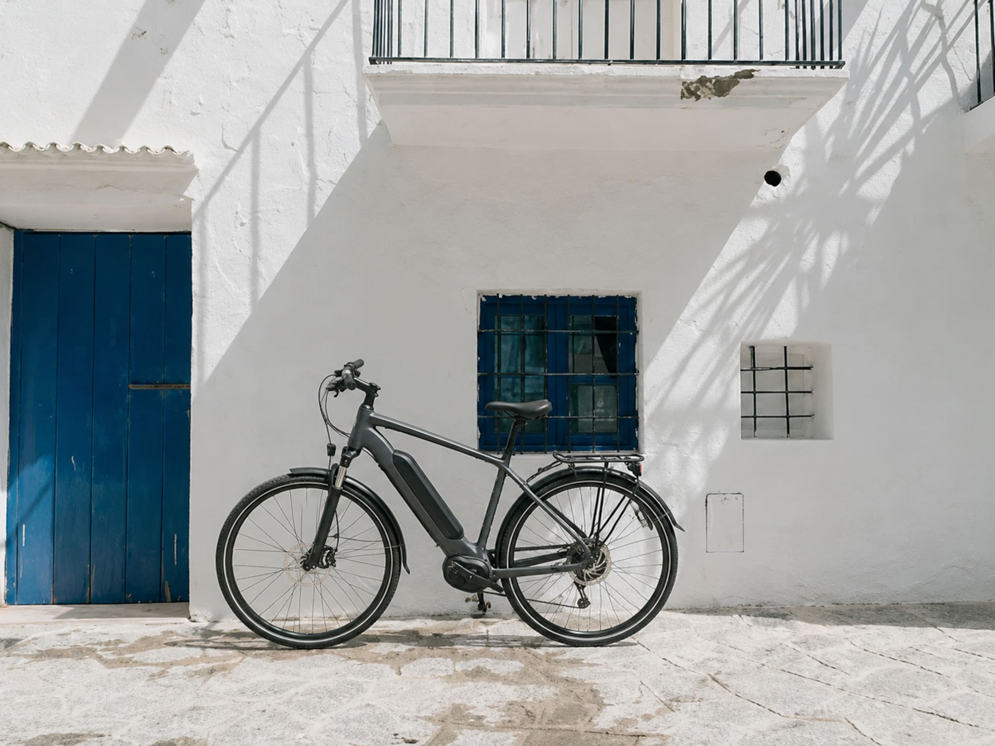 Modern e-bike parked against a white Mediterranean building with blue door.