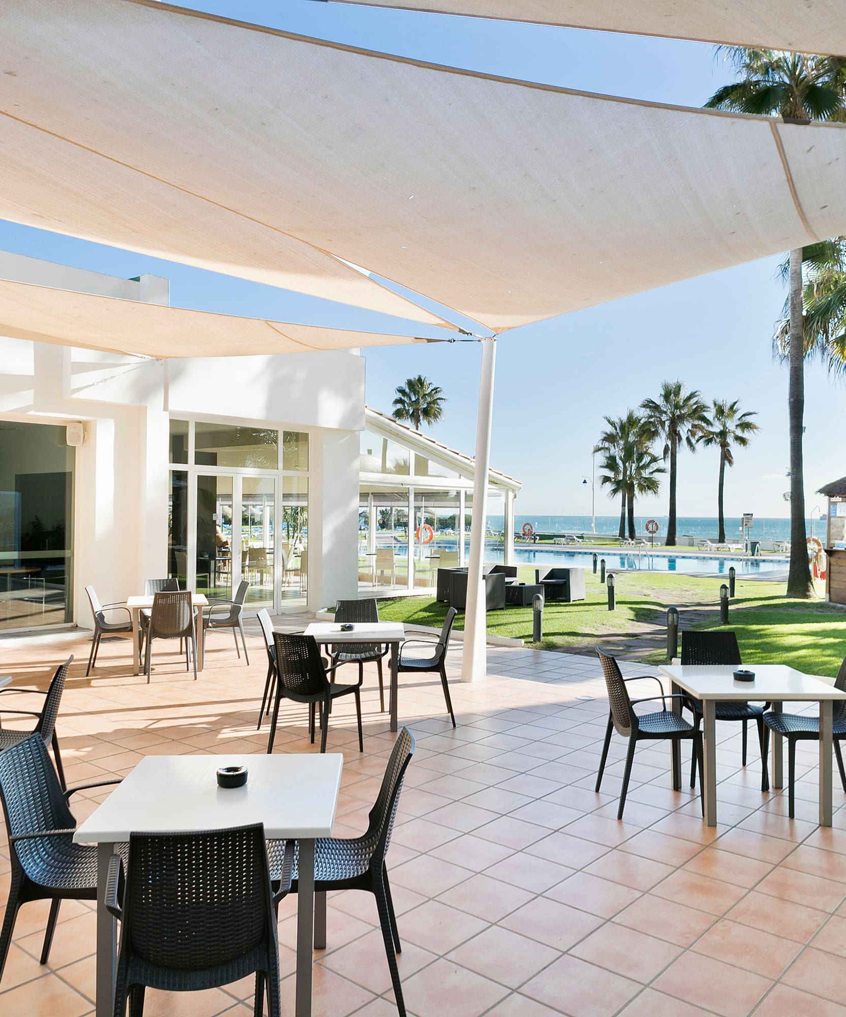 Outdoor hotel patio dining with pool, palm trees, and ocean view.
