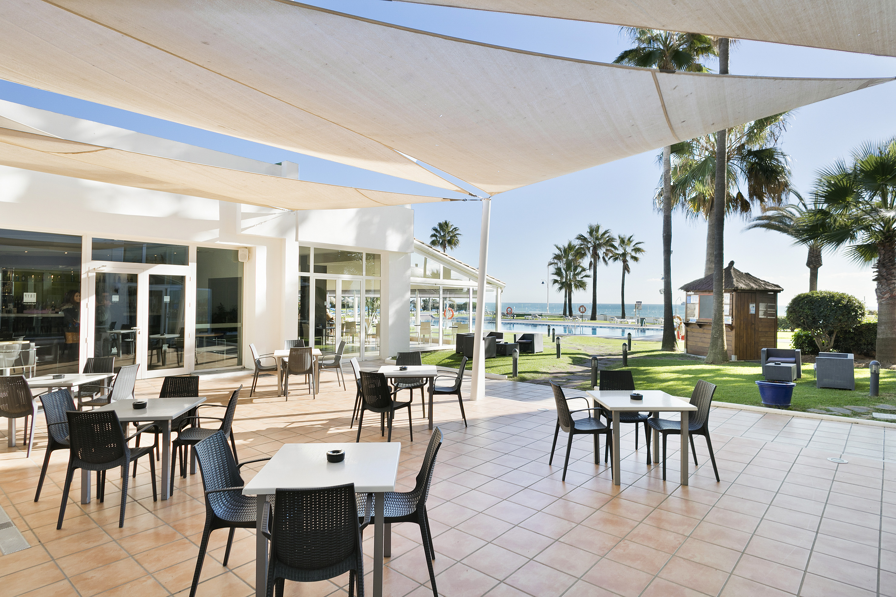 Outdoor hotel patio dining with pool, palm trees, and ocean view.