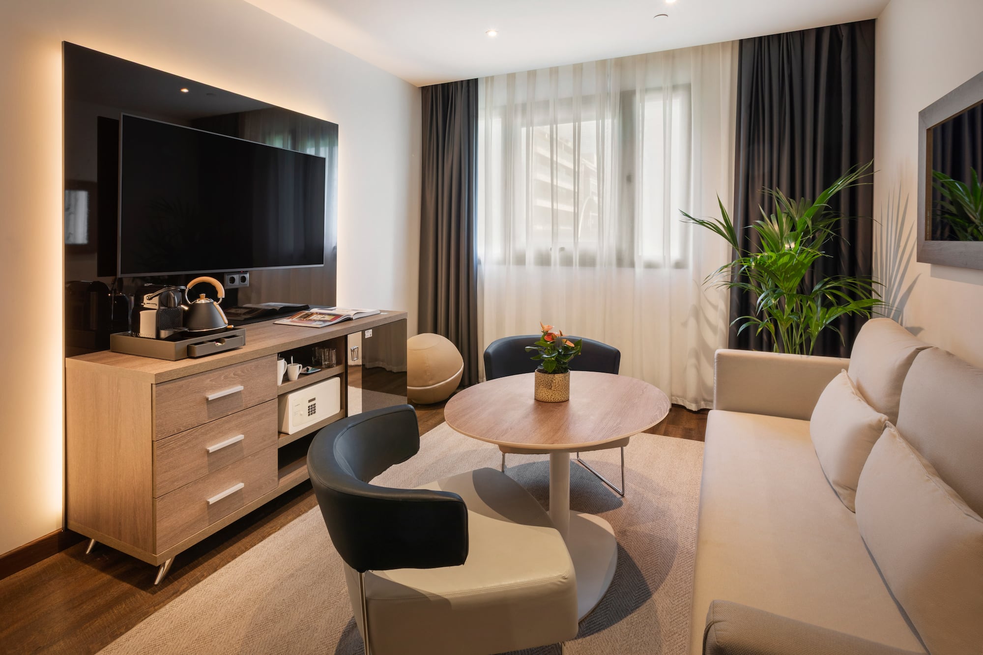 Moderna sala de estar de hotel con TV, sofá, sillones, mesa y cafetera.