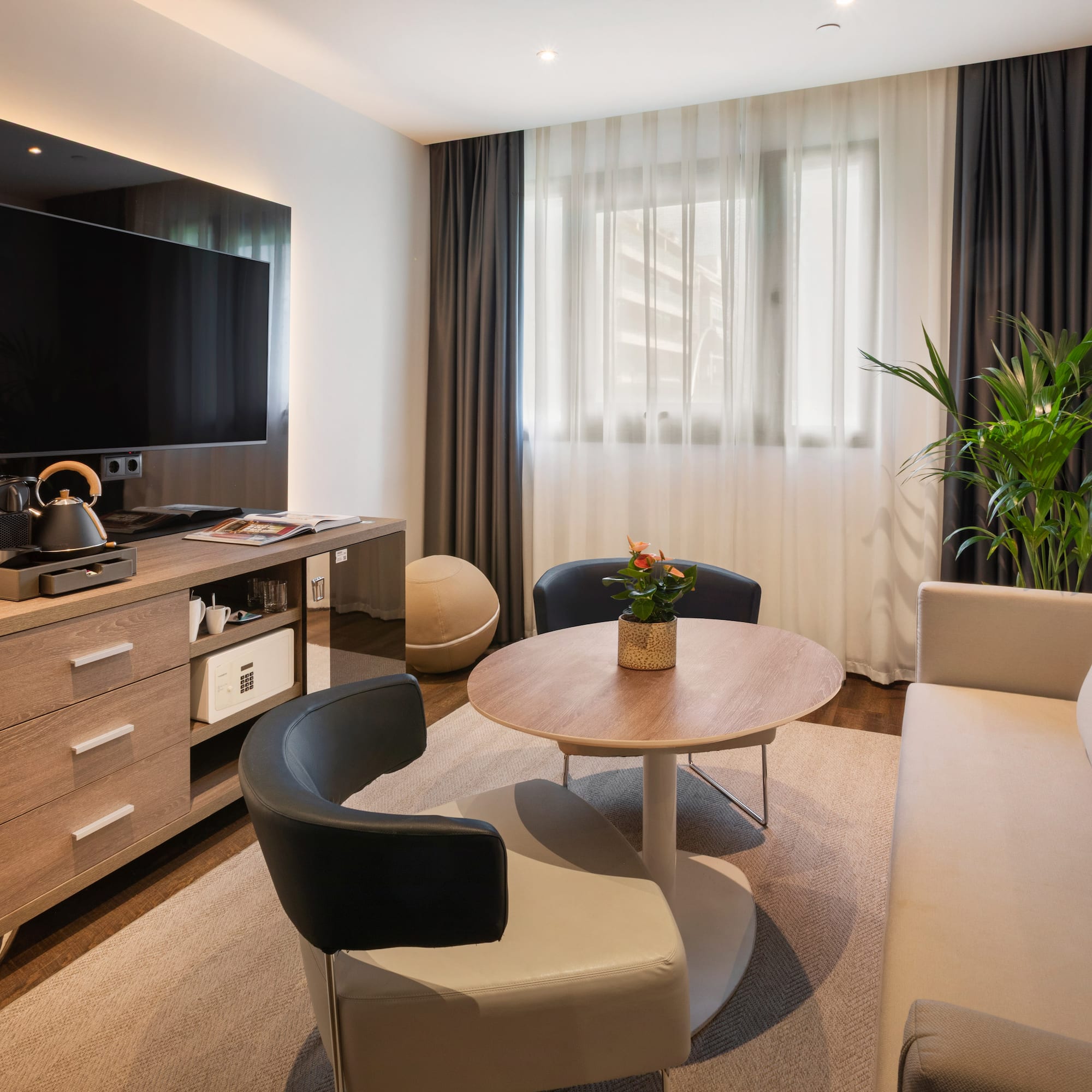 Moderna sala de estar de hotel con TV, sofá, sillones, mesa y cafetera.