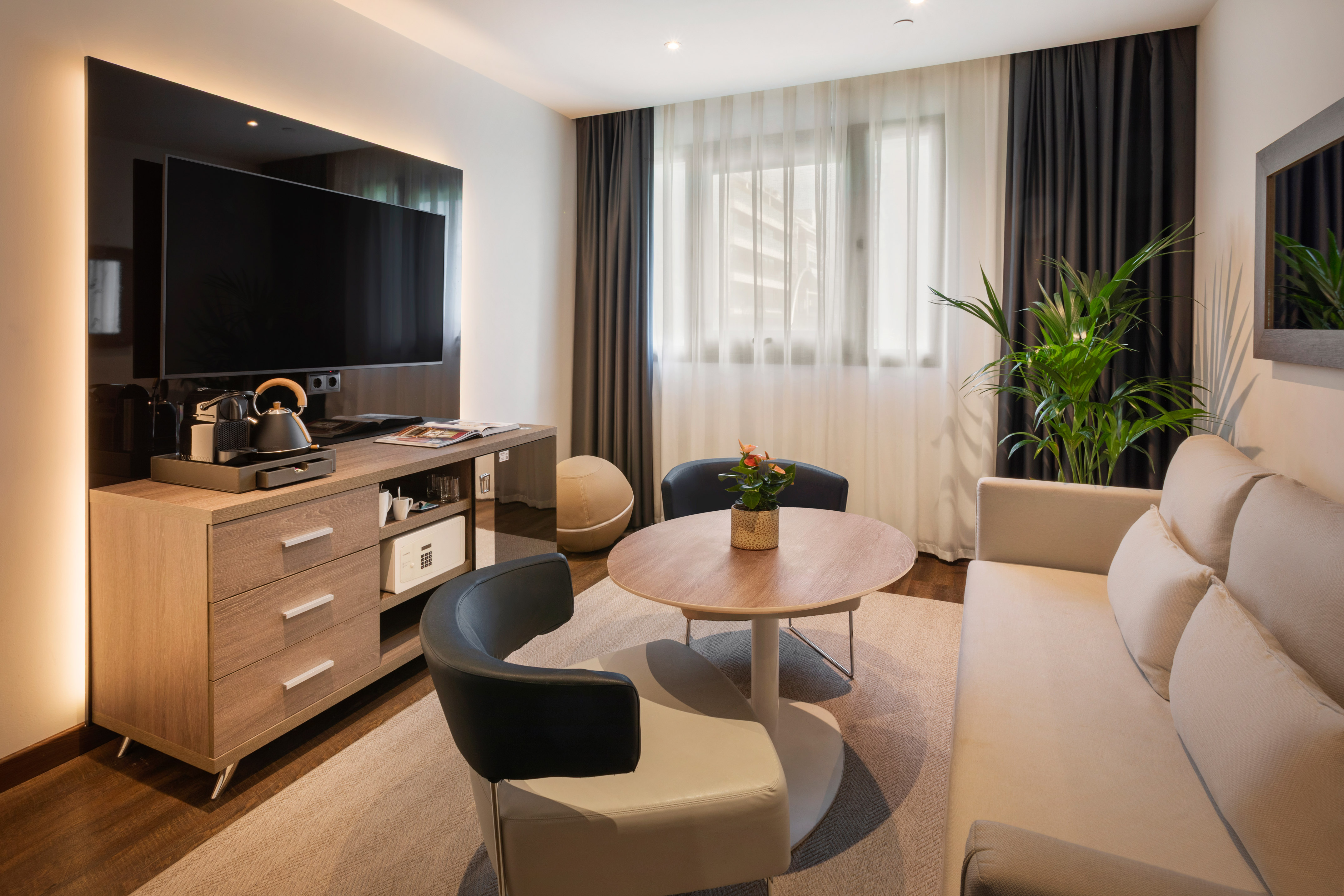 Moderna sala de estar de hotel con TV, sofá, sillones, mesa y cafetera.