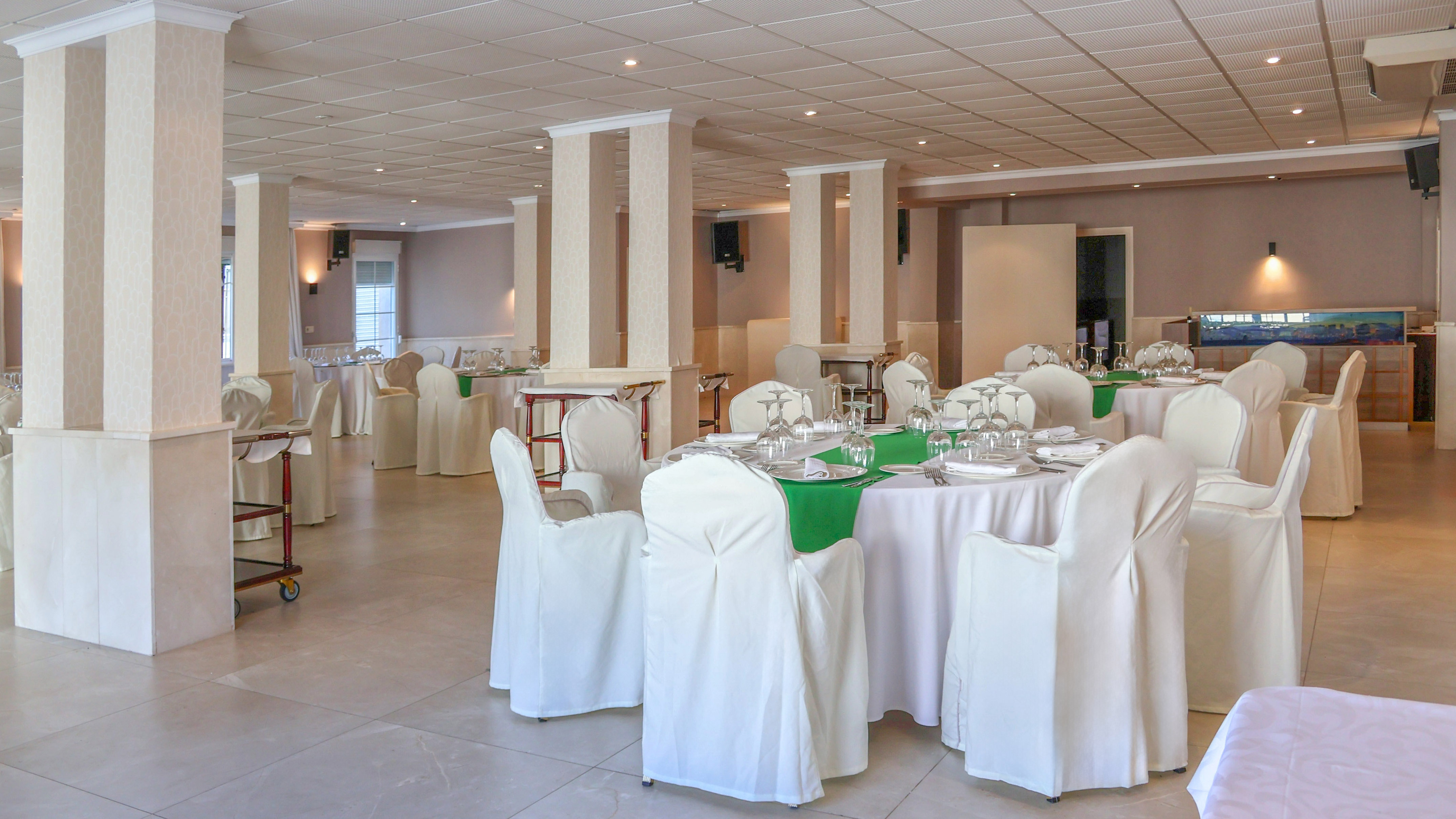 Formal banquet hall with white tables, green runners, and white covered chairs.