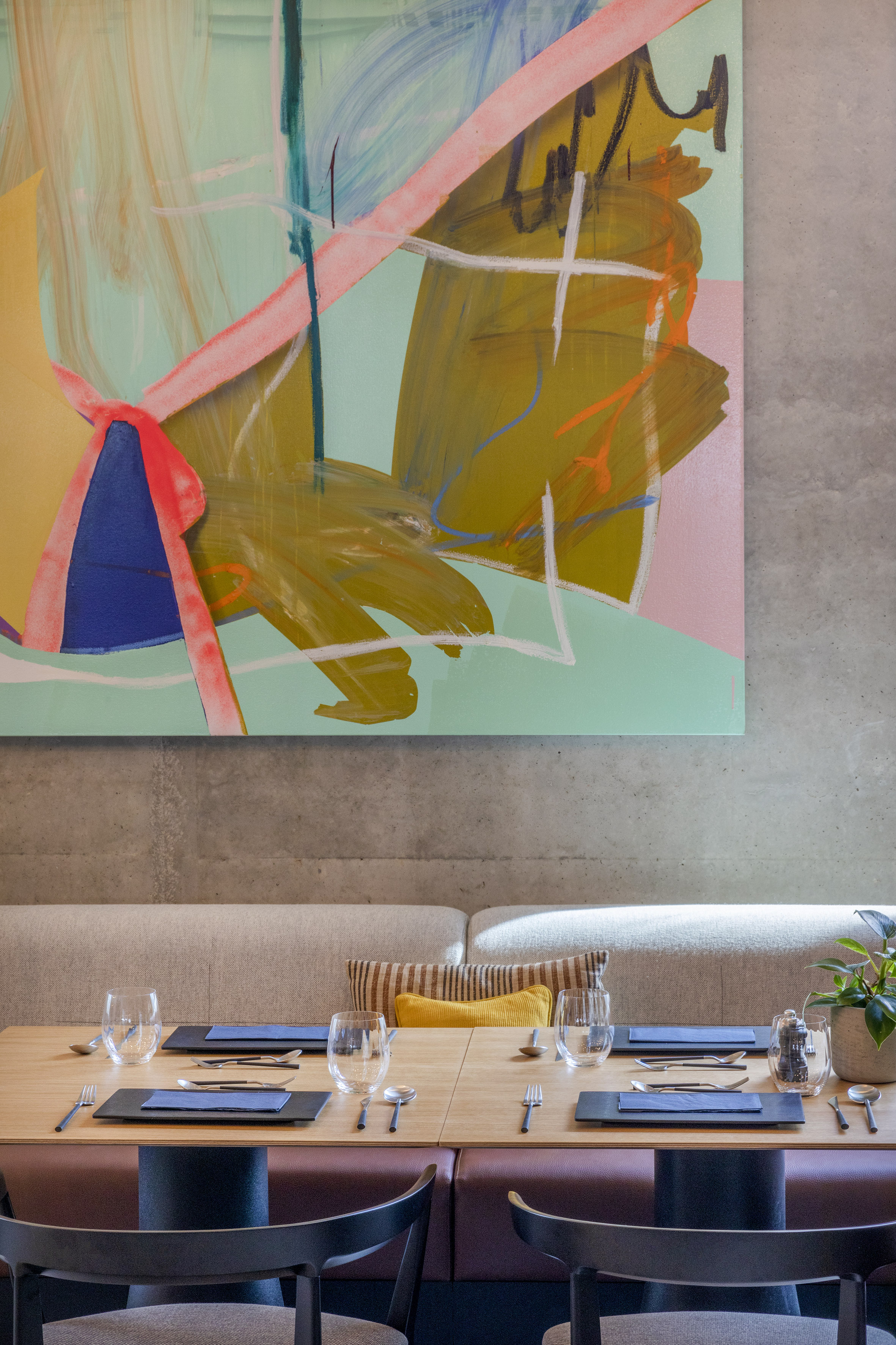 Modern restaurant interior with set tables and a vibrant abstract painting.