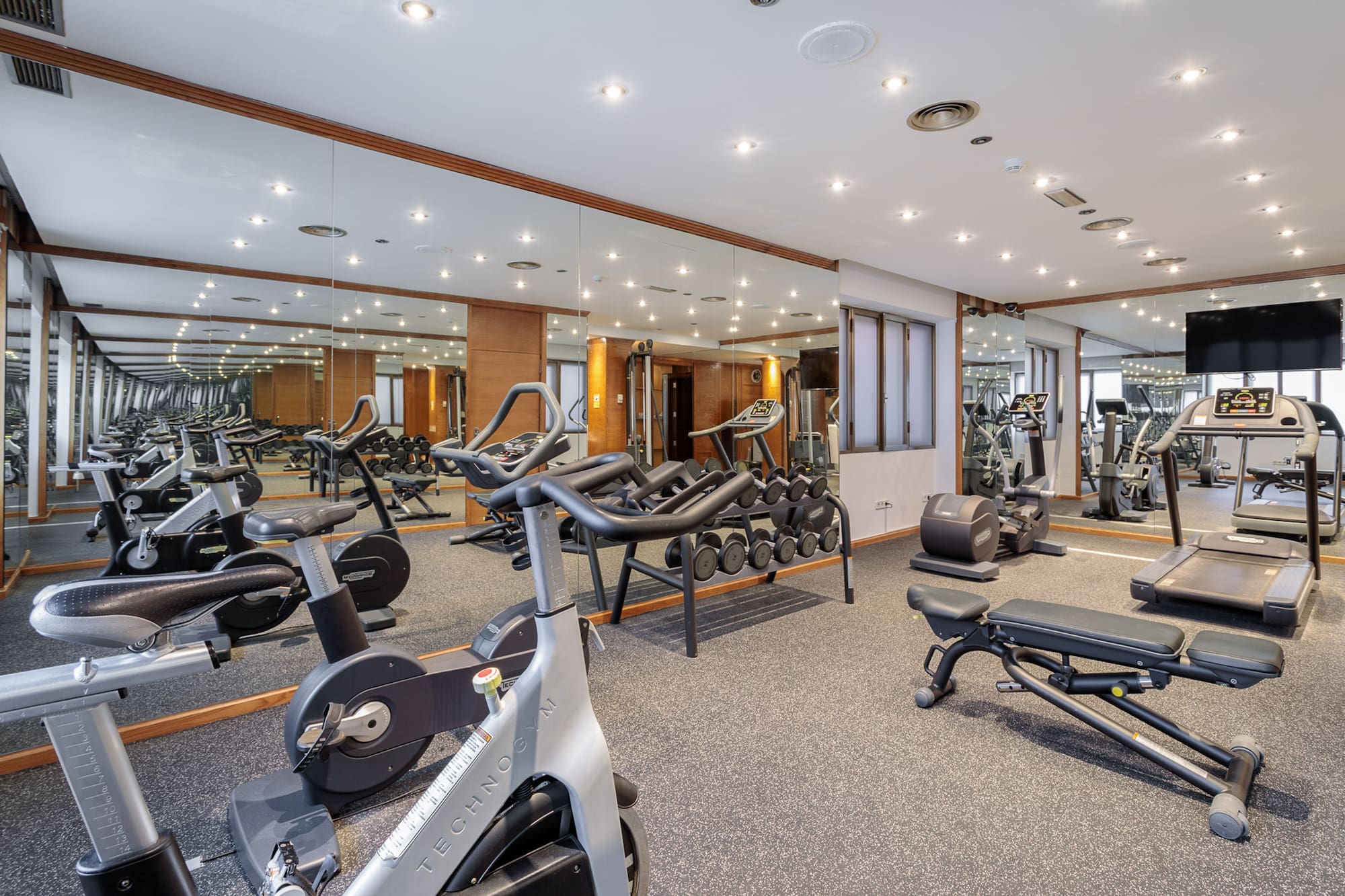 Modern gym with stationary bikes, treadmills, elliptical, dumbbells, and mirrors.