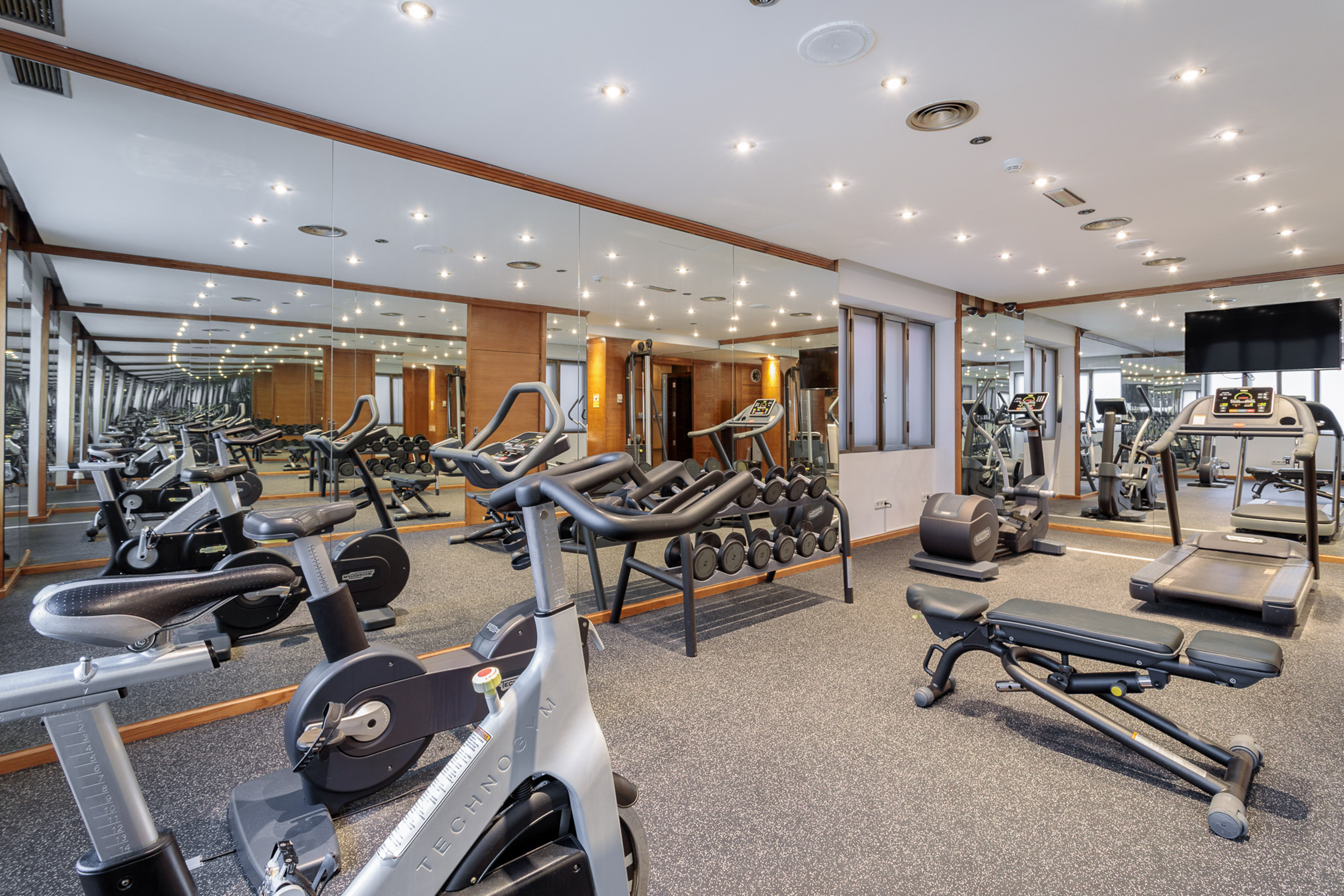 Modern gym with stationary bikes, treadmills, elliptical, dumbbells, and mirrors.