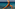 Woman in brown yoga jumpsuit performing Warrior I yoga pose by the turquoise sea.