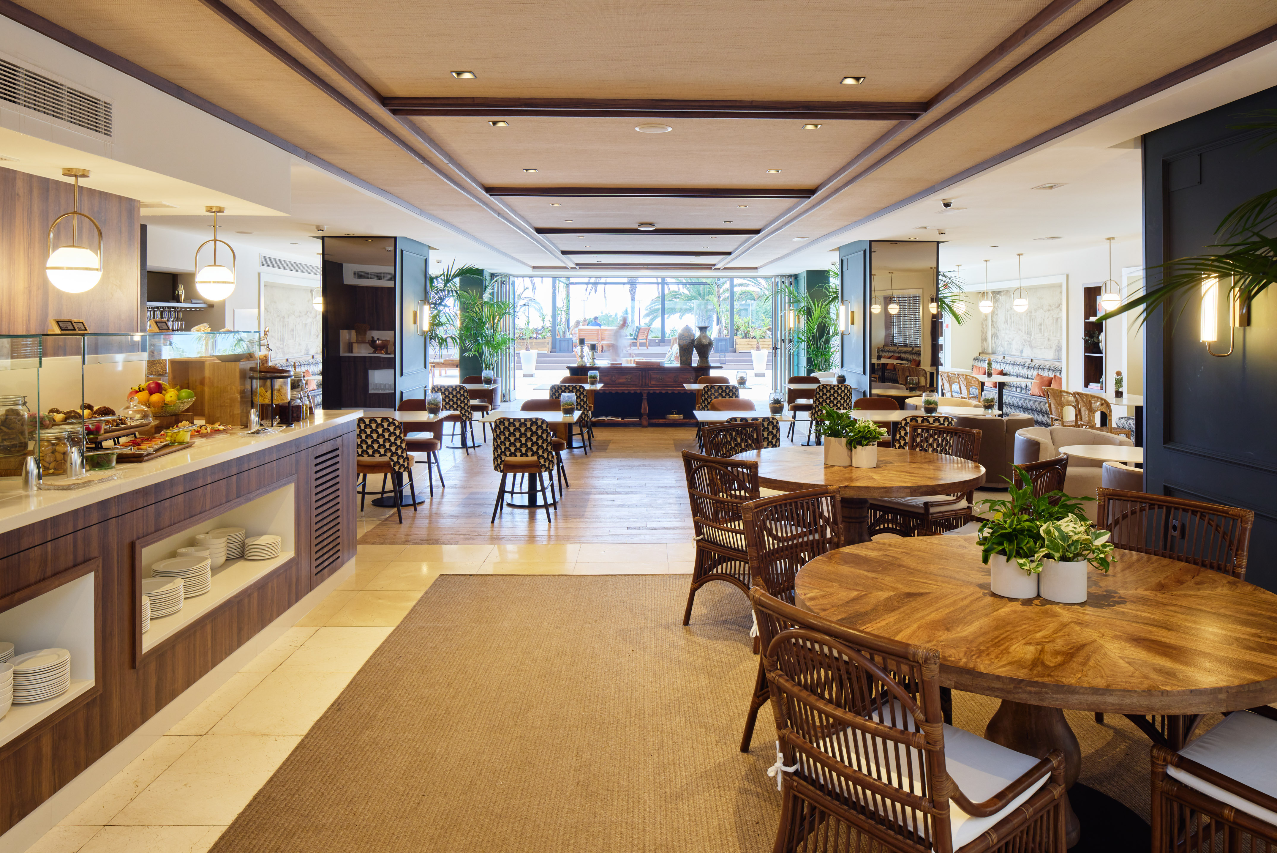 Modern hotel restaurant with breakfast buffet, wooden tables, rattan chairs.