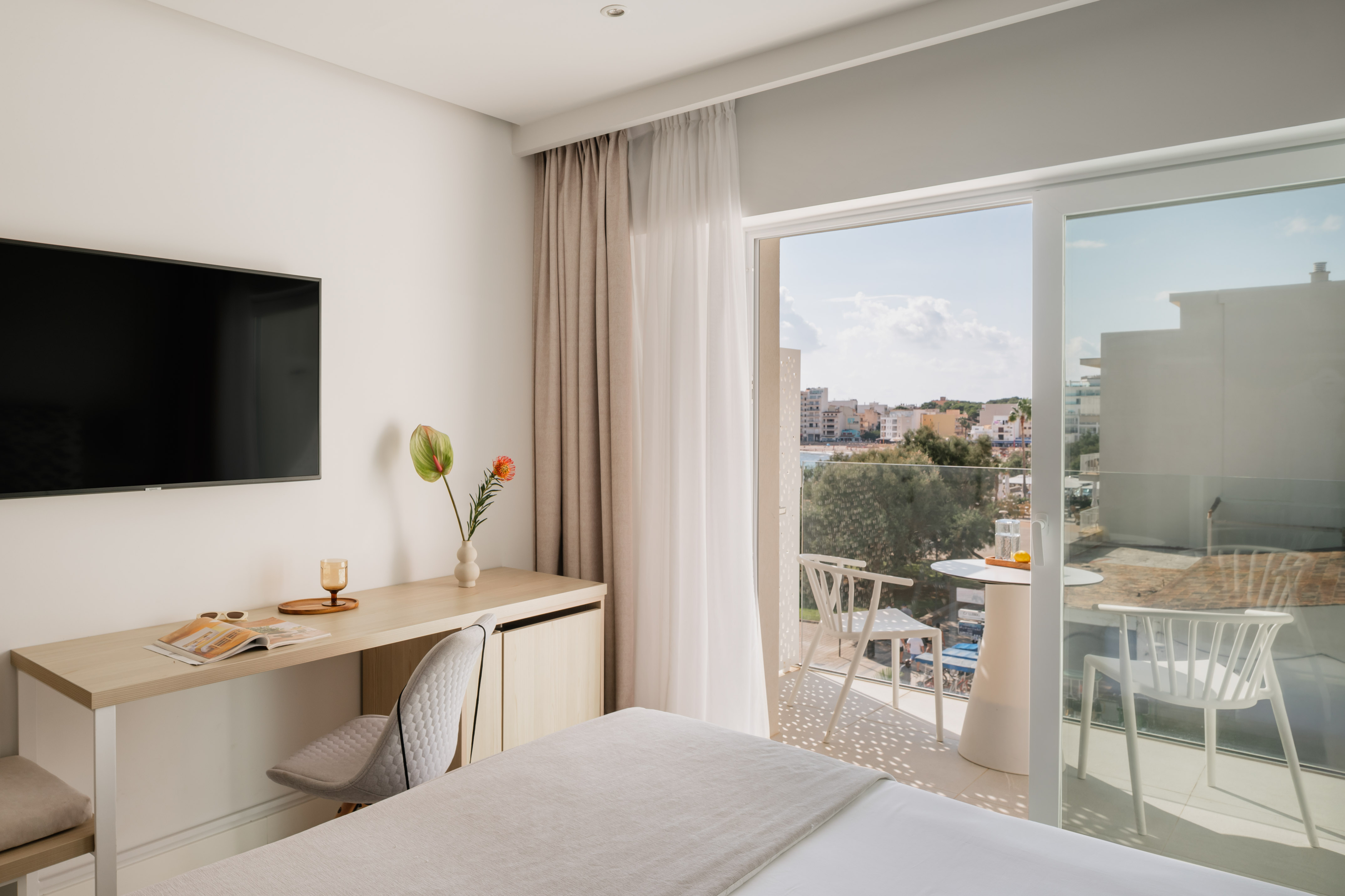 Modern hotel room with desk, TV, comfy bed, and balcony with ocean view.