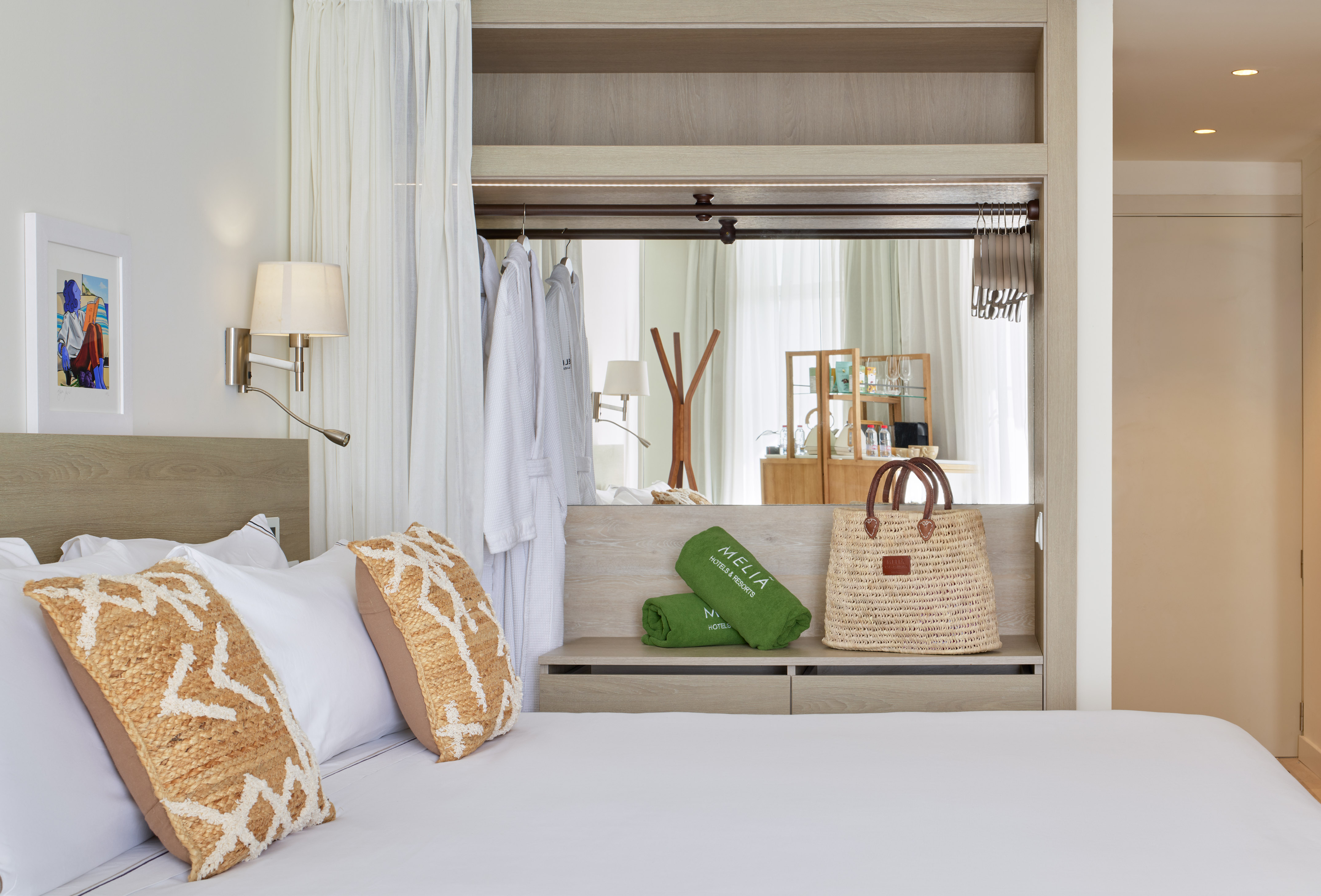 Modern Meliá hotel bedroom with white bed, textured pillows, robes, and green towels.