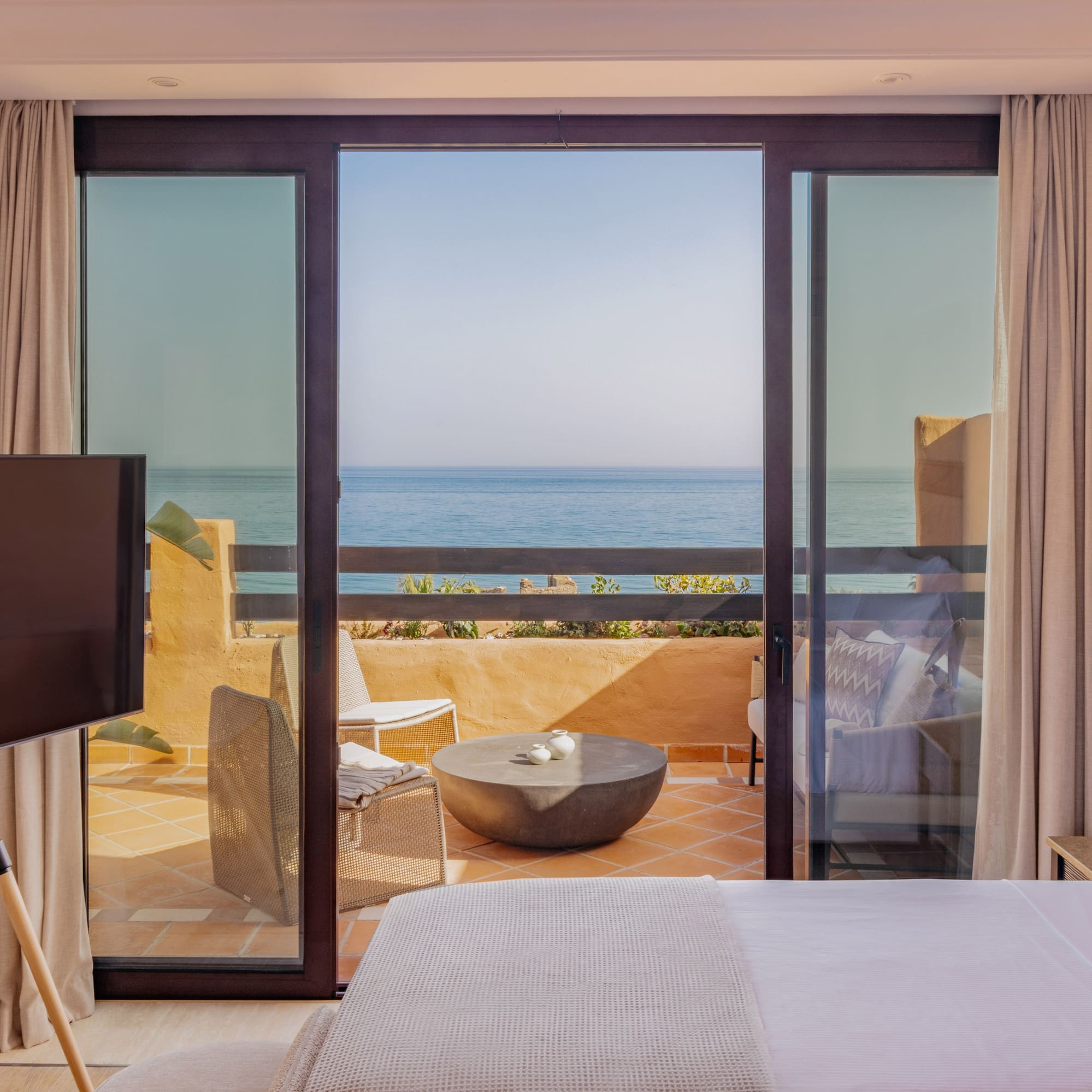 Luxury hotel bedroom with ocean view balcony and outdoor seating.