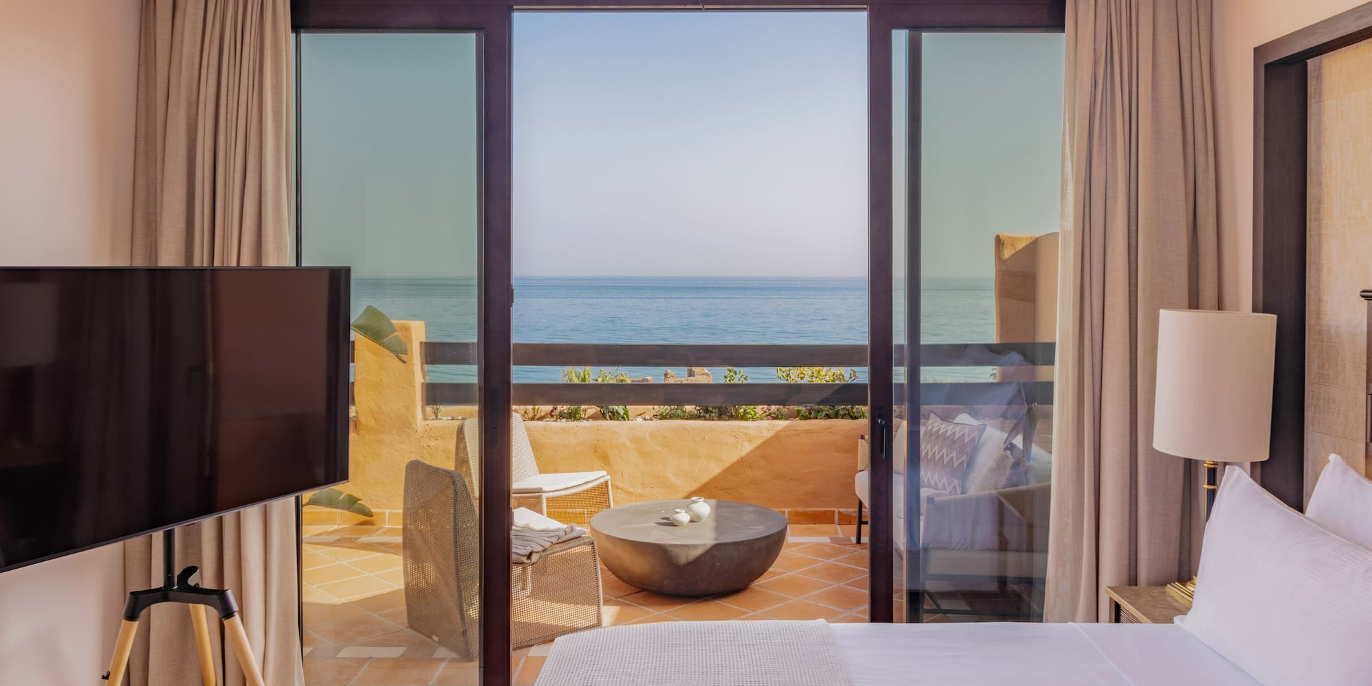 Luxury hotel bedroom with ocean view balcony and outdoor seating.