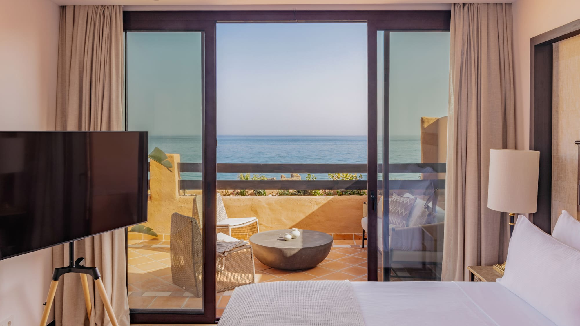 Luxury hotel bedroom with ocean view balcony and outdoor seating.
