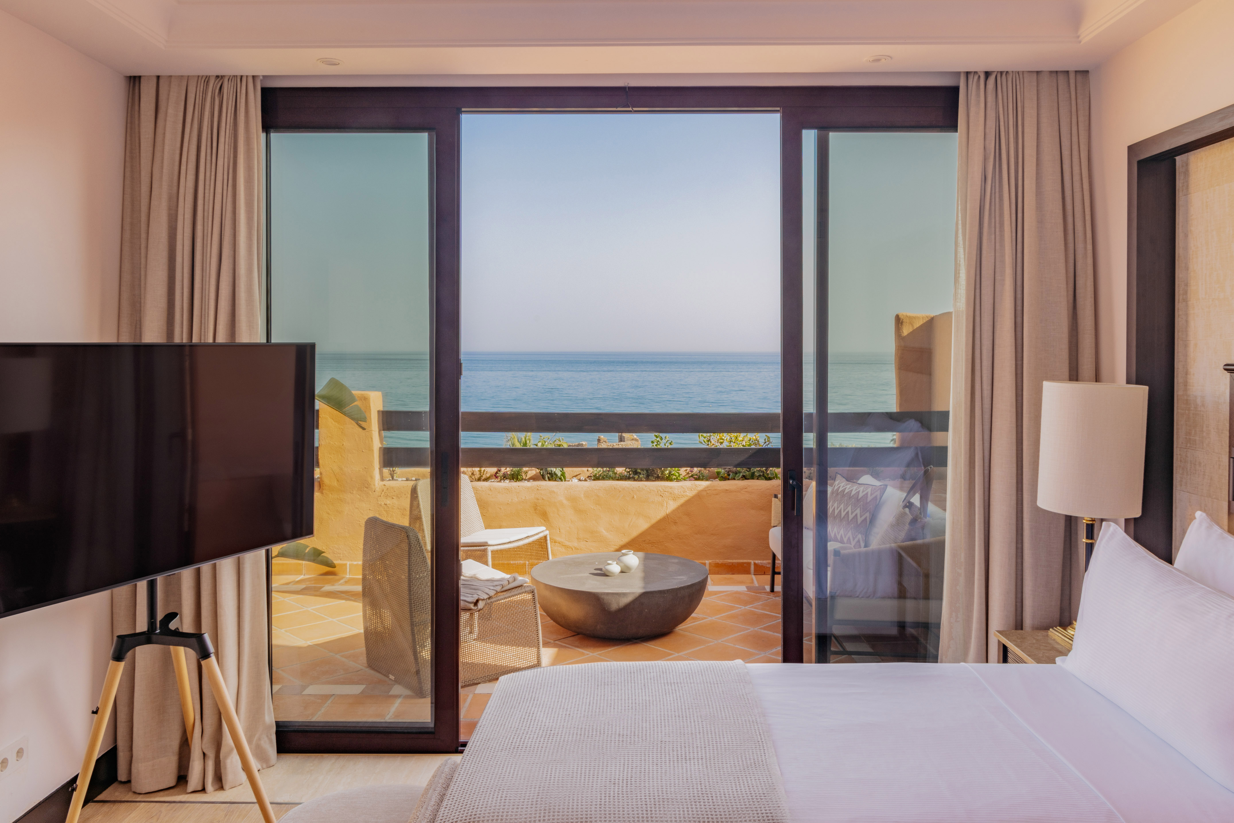 Luxury hotel bedroom with ocean view balcony and outdoor seating.