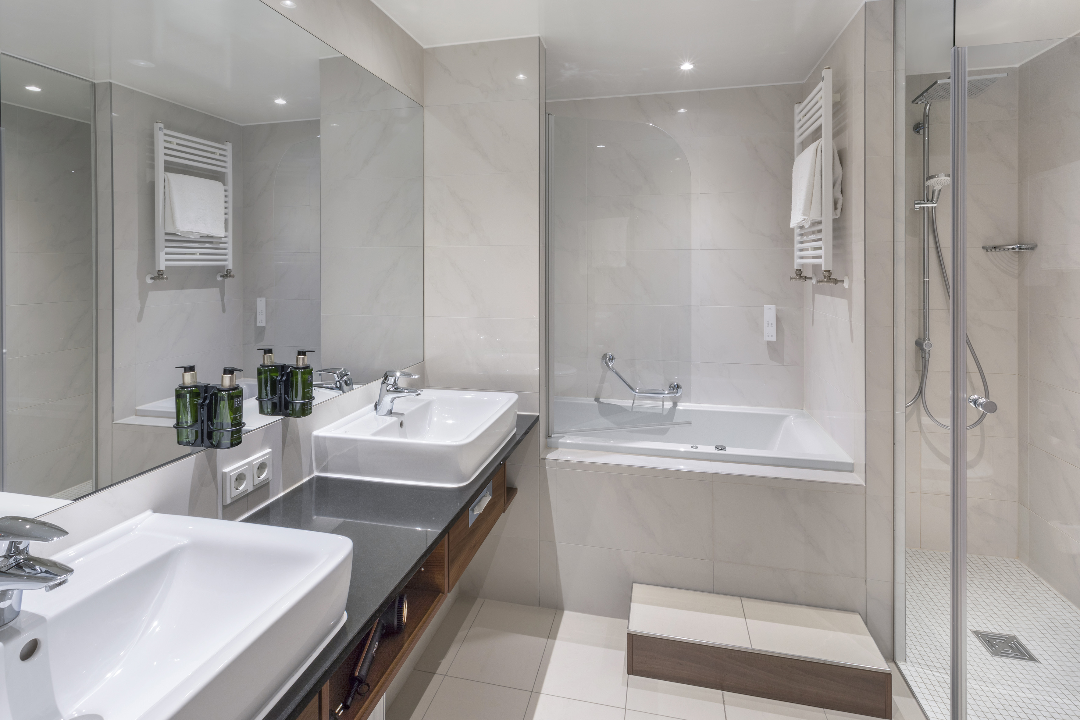 Modern bathroom with double sink vanity, integrated bathtub, and glass shower.