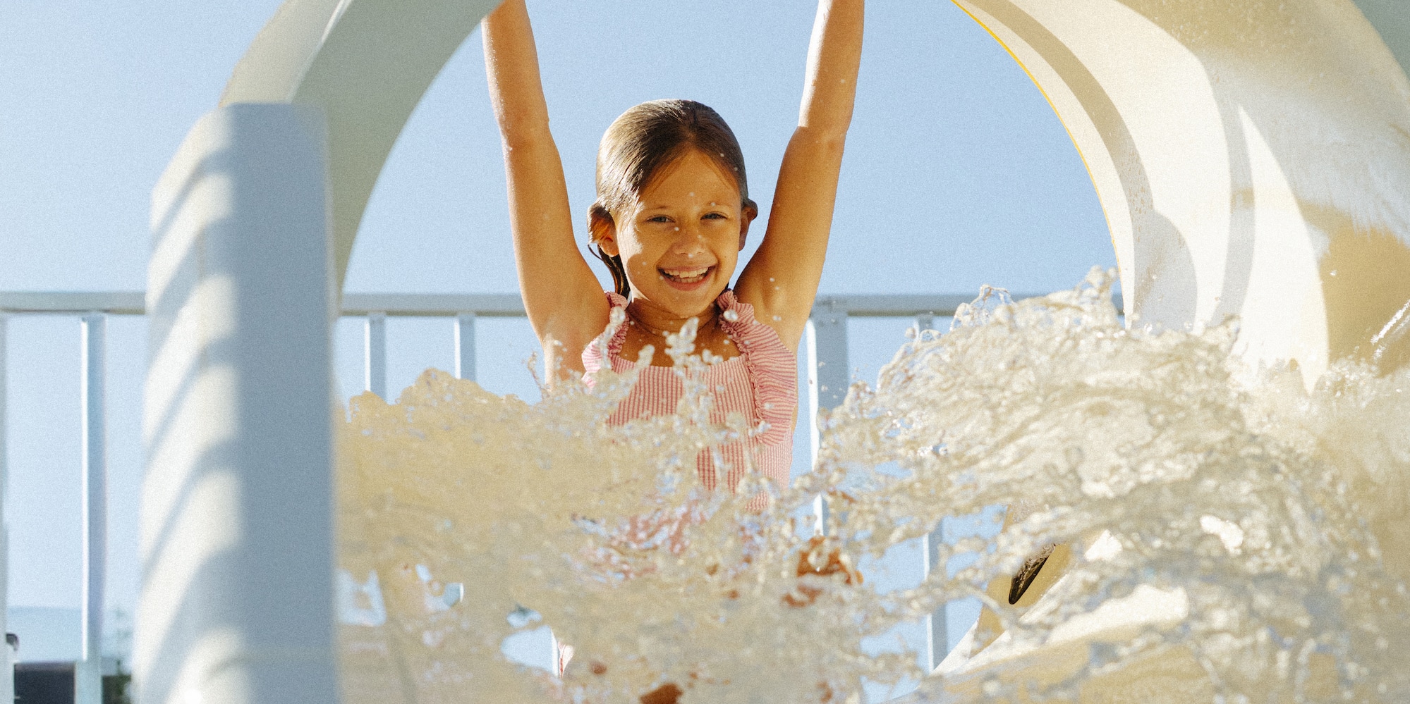 Smiling girl splashing down a water slide at a summer water park.