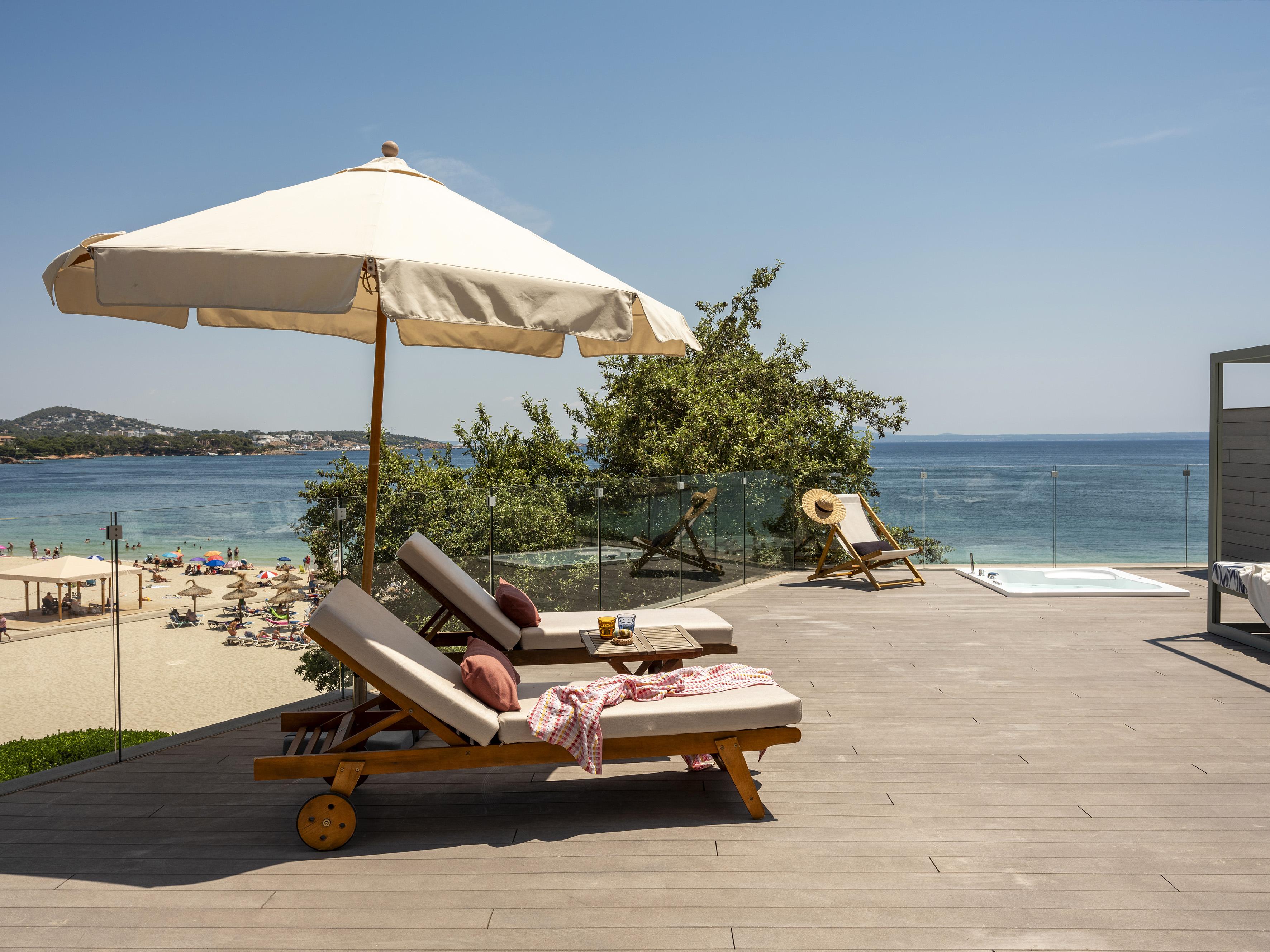 Ocean view deck with sun loungers, umbrella, jacuzzi, and sandy beach below.
