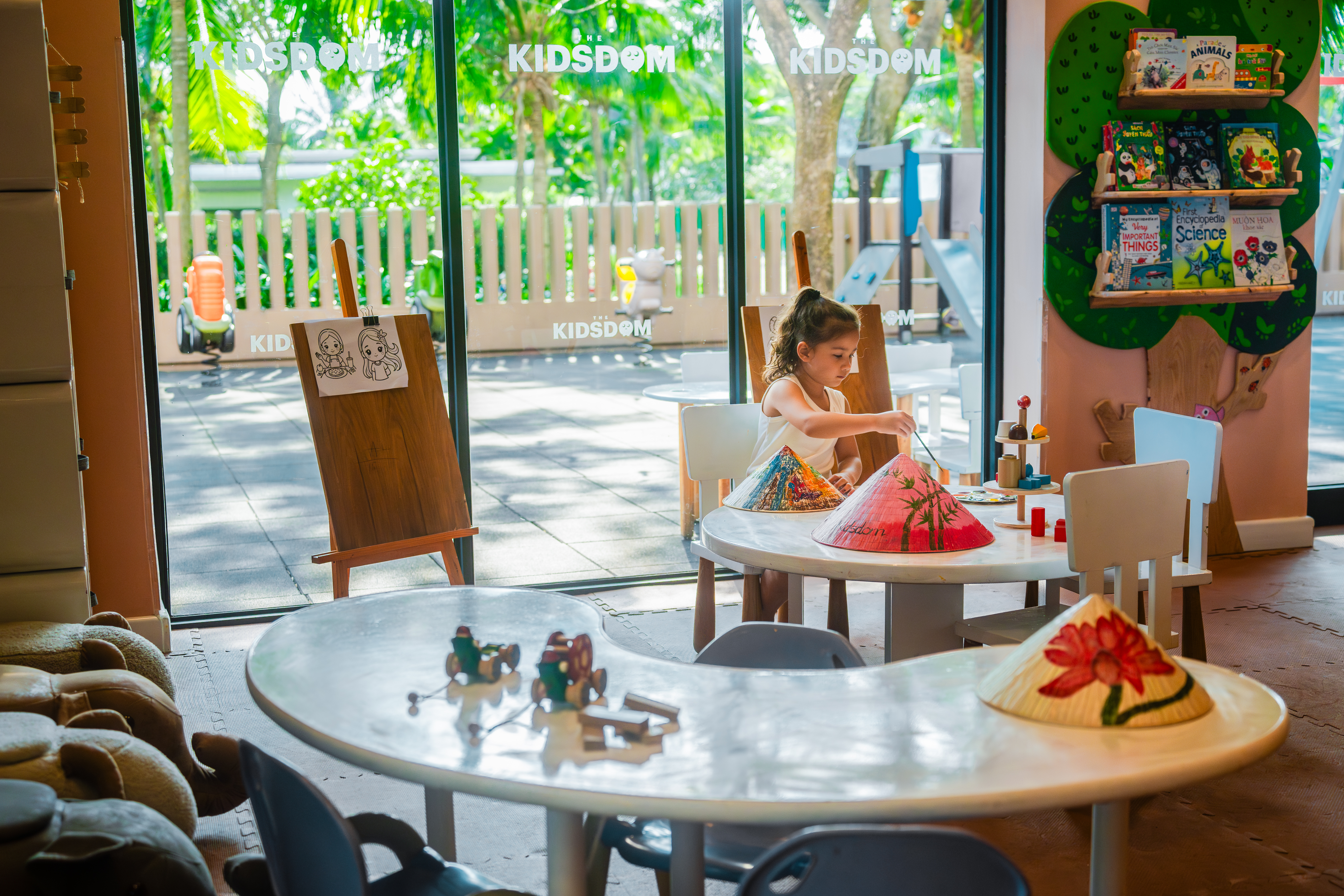 Girl painting colorful conical hats in a bright Kidsdom children's play area.