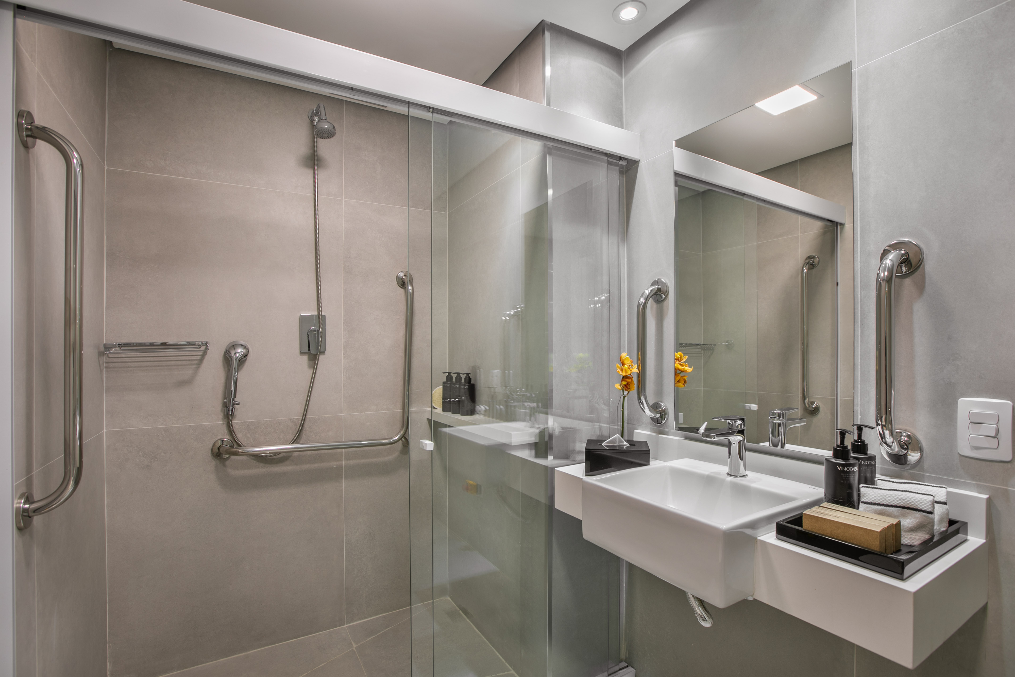 Accessible bathroom with modern shower, grab bars, sink, and grey tiles.
