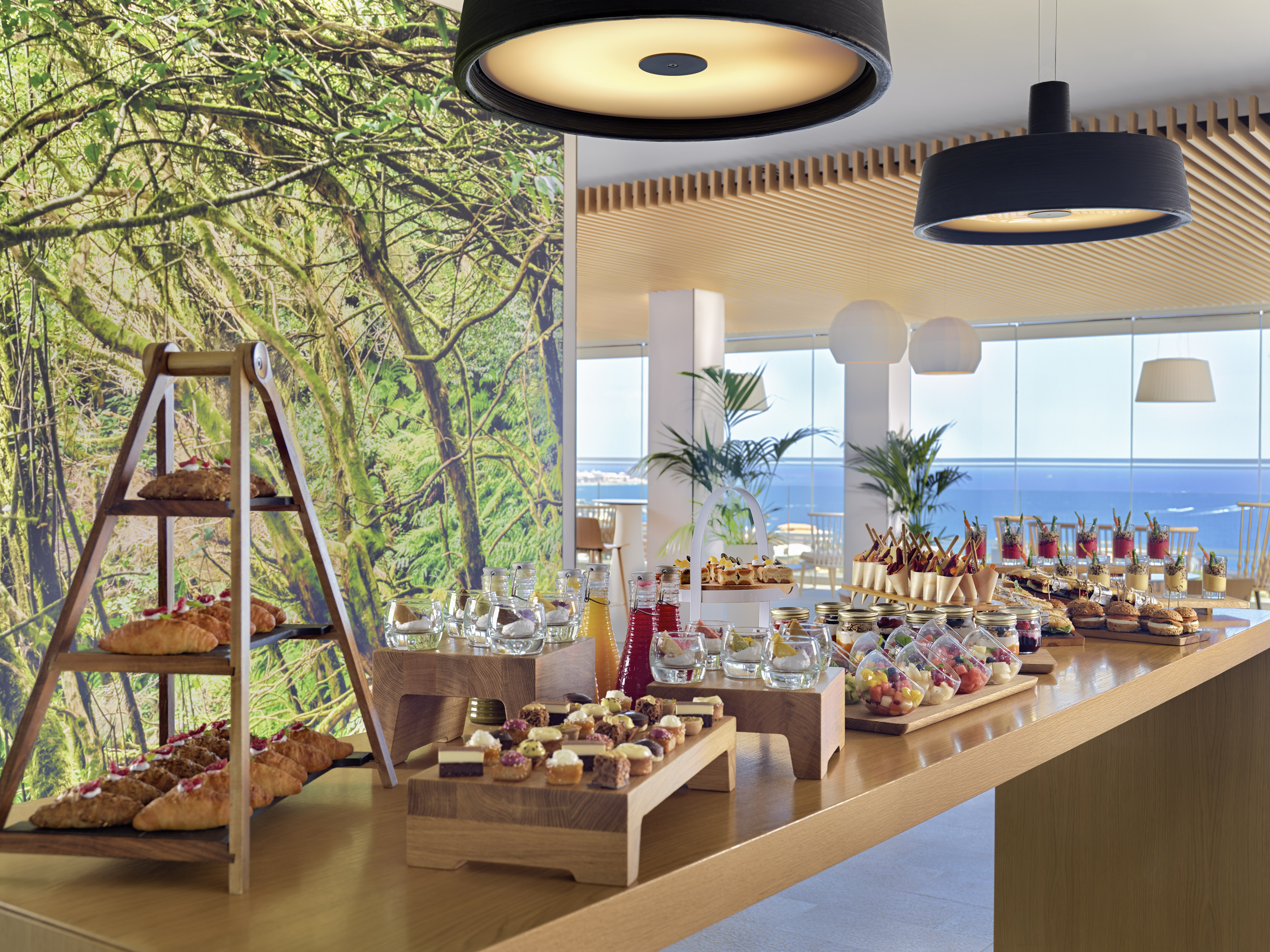Modern hotel buffet with pastries, desserts, fruit, and ocean view.