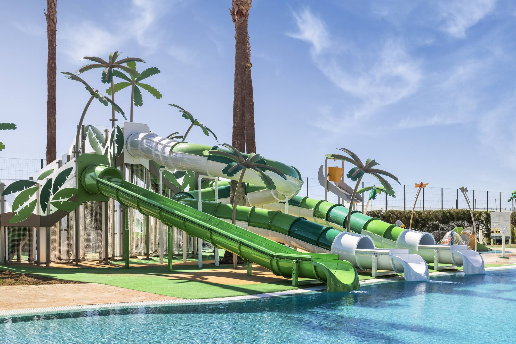 Sunny resort water park with green slides, palm trees, and pool.