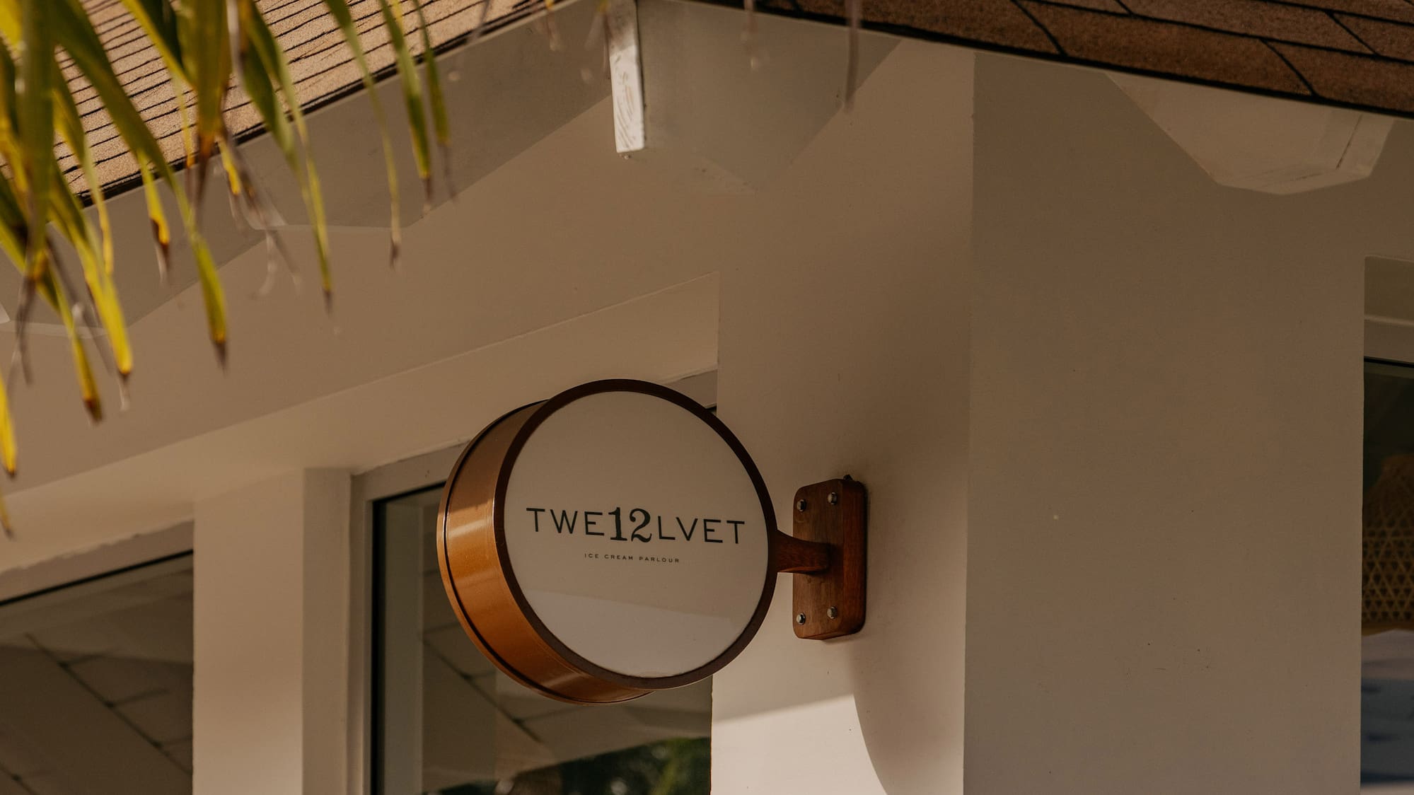 TWE12LVET Ice Cream Parlour sign on white building with palm leaves.