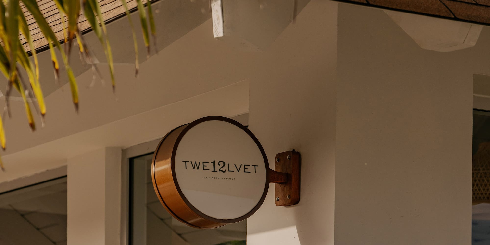 TWE12LVET Ice Cream Parlour sign on white building with palm leaves.