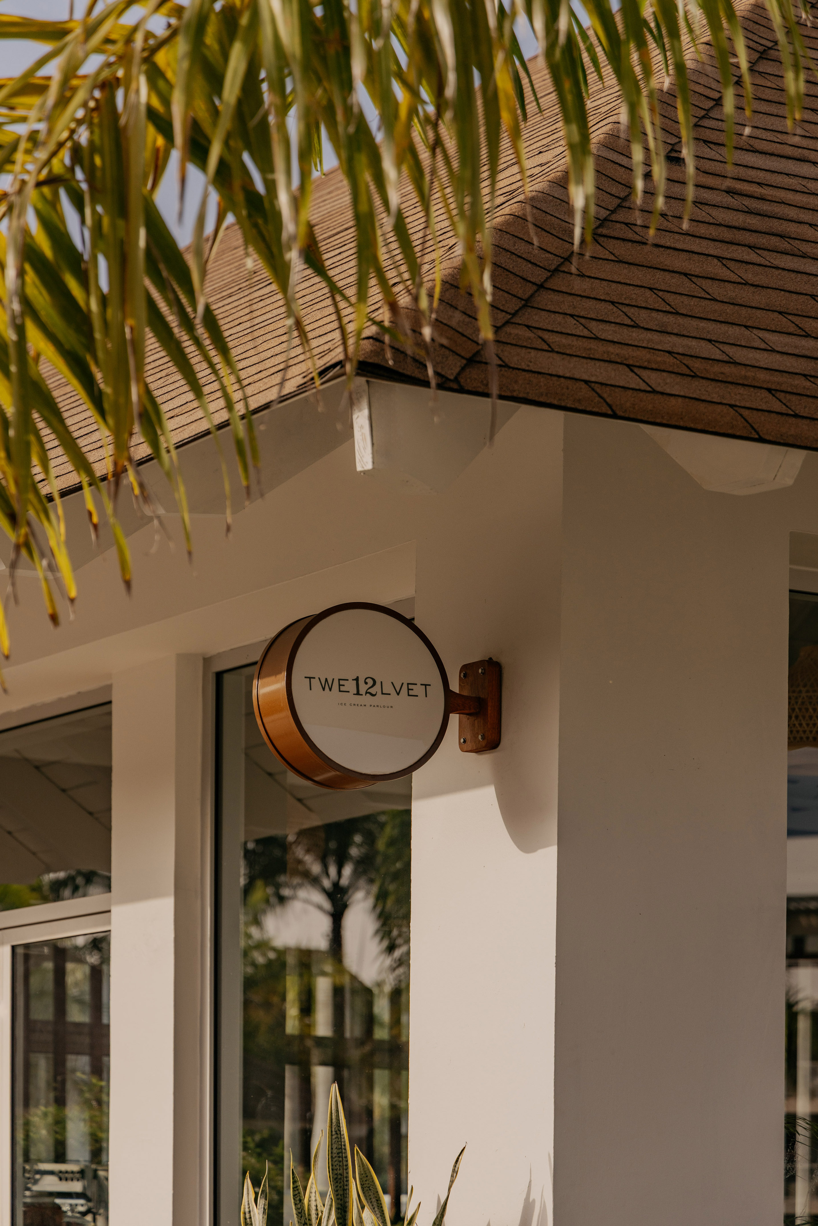 TWE12LVET Ice Cream Parlour sign on white building with palm leaves.