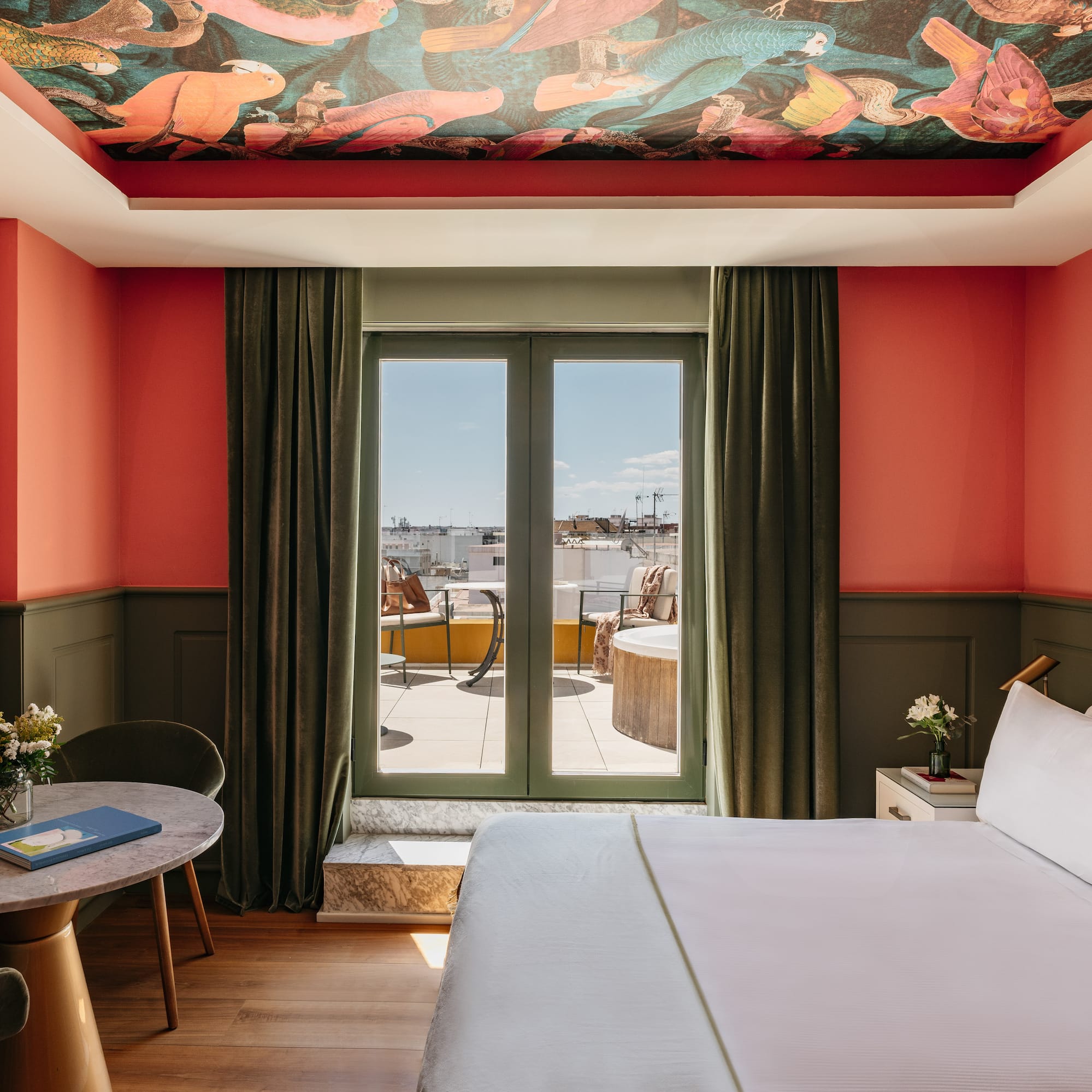 Suite de hotel colorida con mural techo, paredes coral y balcón privado.