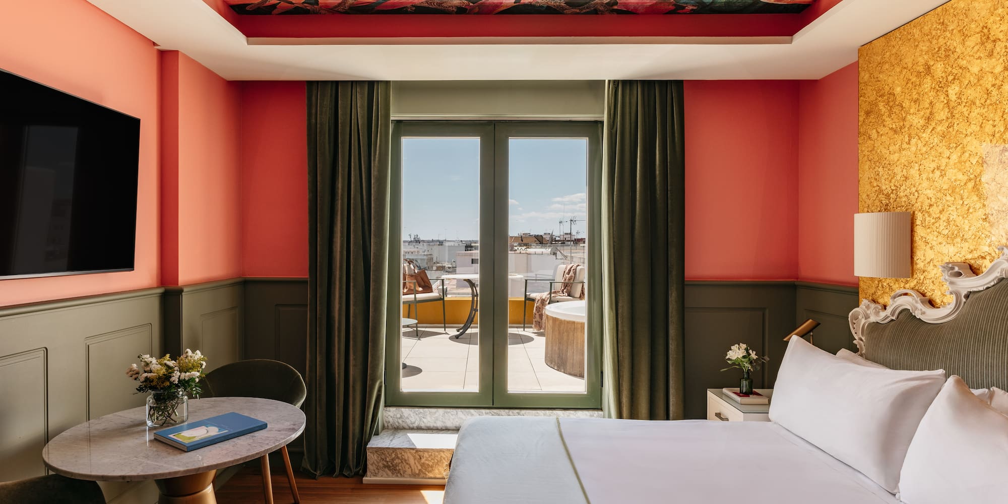 Suite de hotel colorida con mural techo, paredes coral y balcón privado.