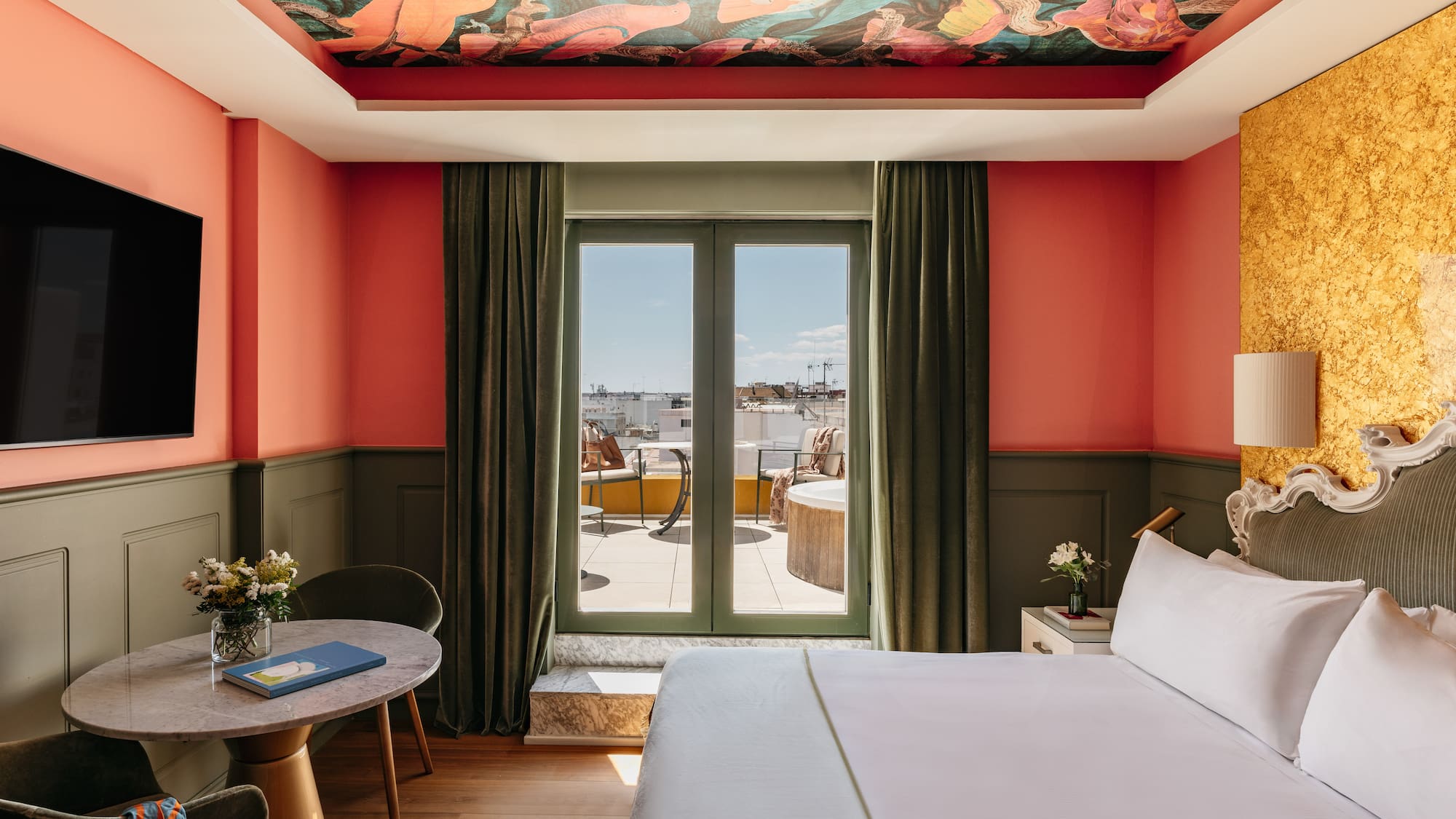 Suite de hotel colorida con mural techo, paredes coral y balcón privado.