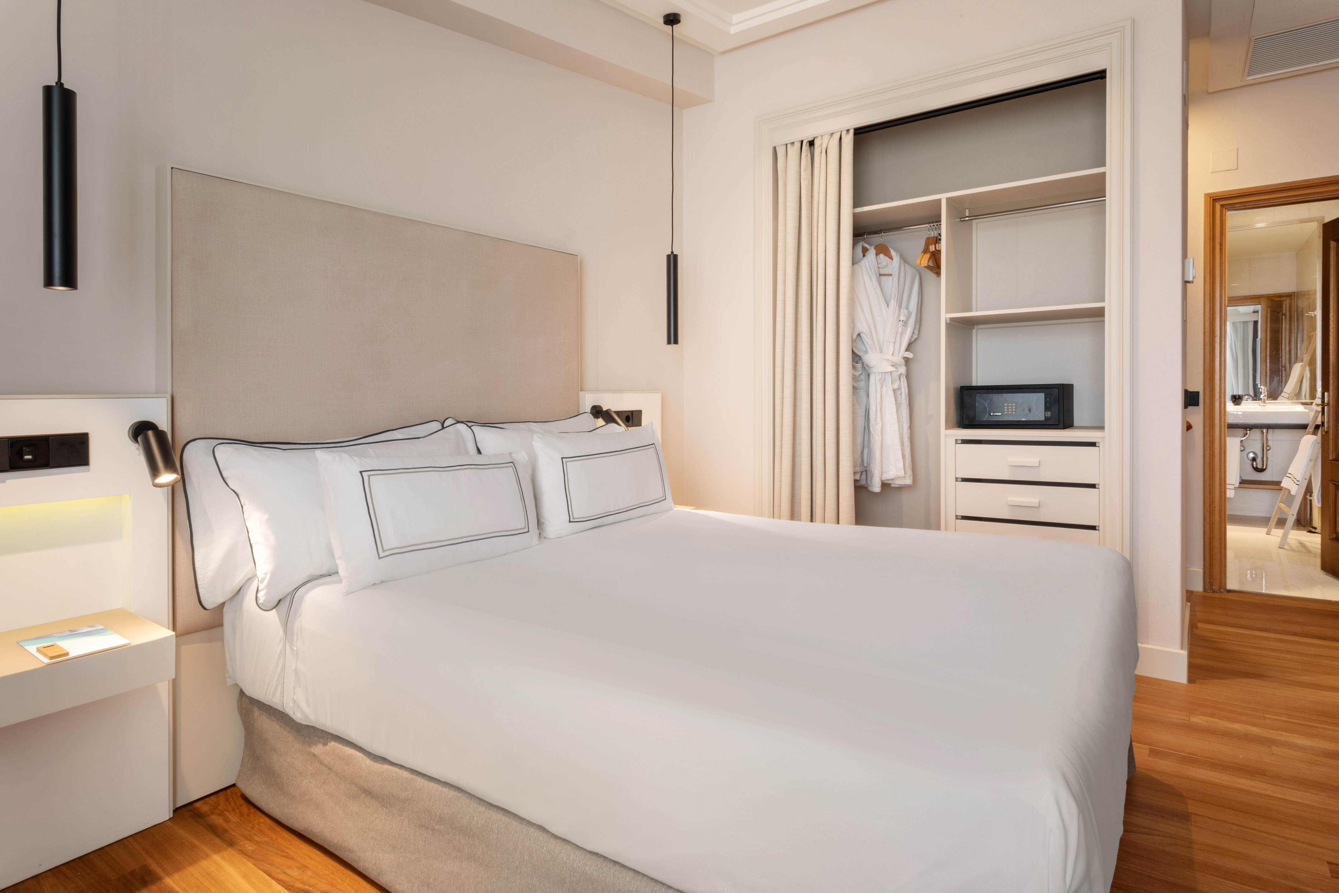 Hotel bedroom with white bed, bedside lamp, and open closet containing a safe.