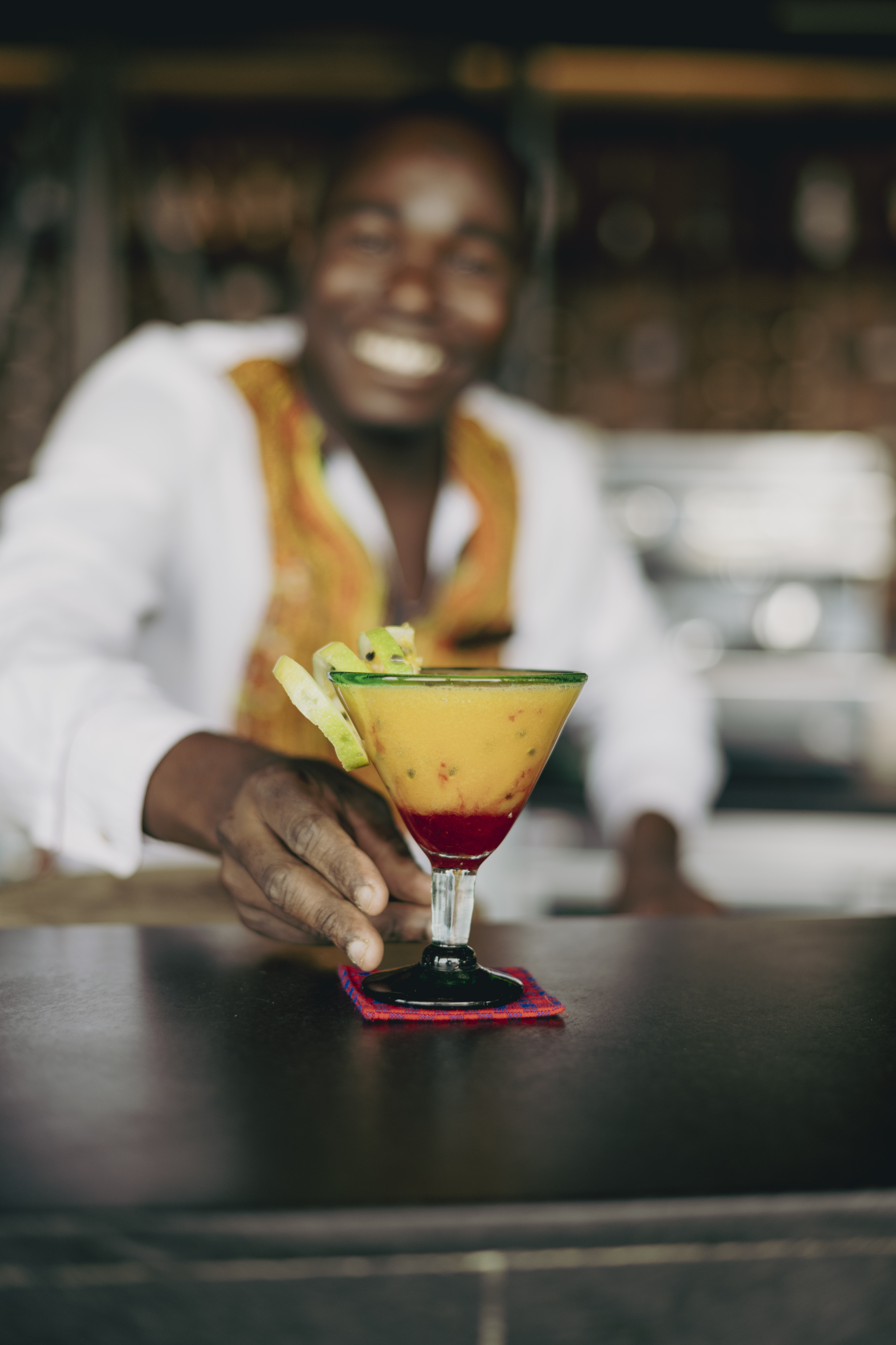 Smiling bartender presenting colorful tropical cocktail with kiwi garnish.