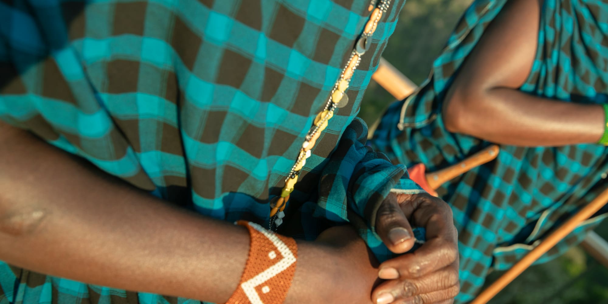 Maasai person's hands wearing orange beaded bracelet and blue plaid shuka.