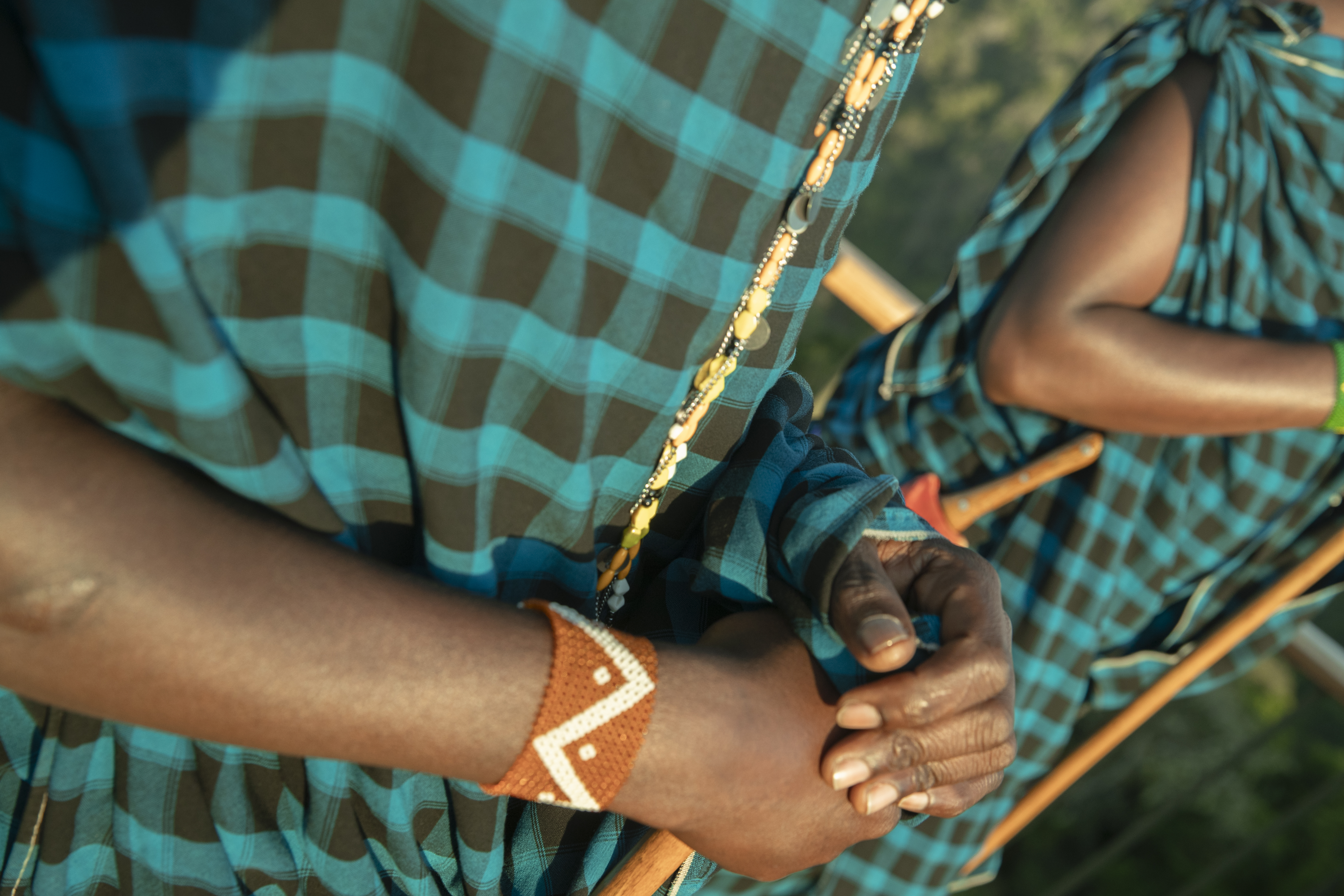 Maasai person's hands wearing orange beaded bracelet and blue plaid shuka.