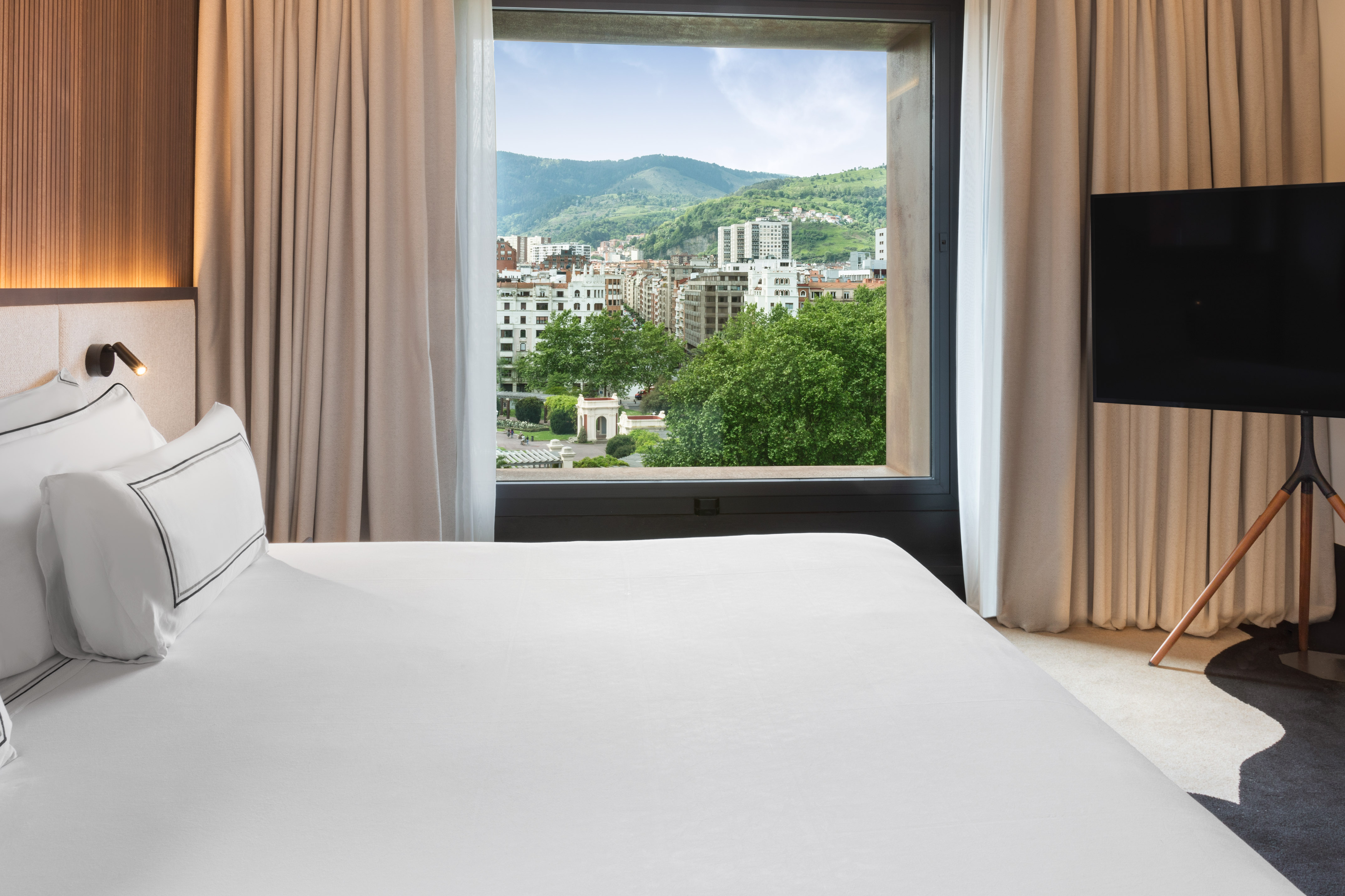 Luxury hotel bedroom with city and mountain view from large window.