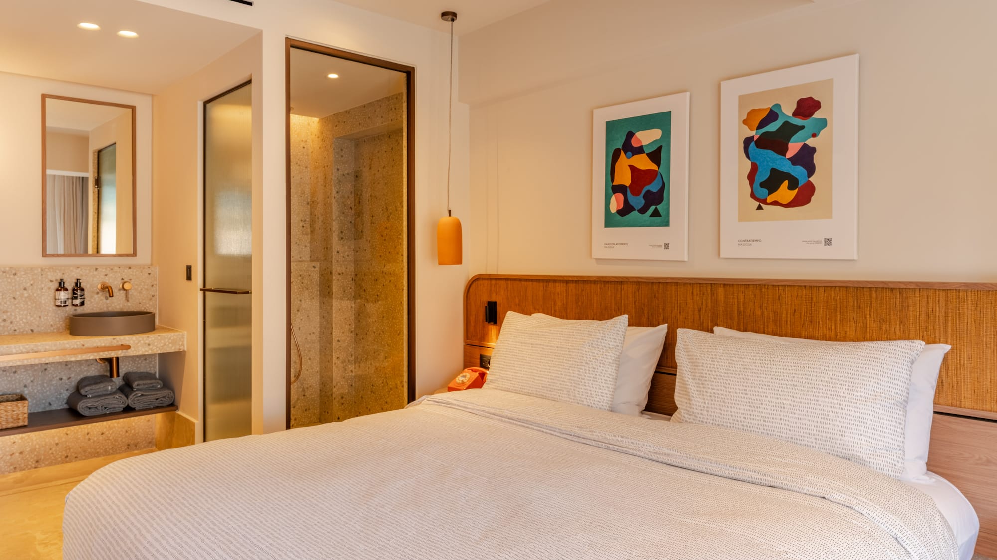 a bed with white sheets and pillows in a room with art on the wall