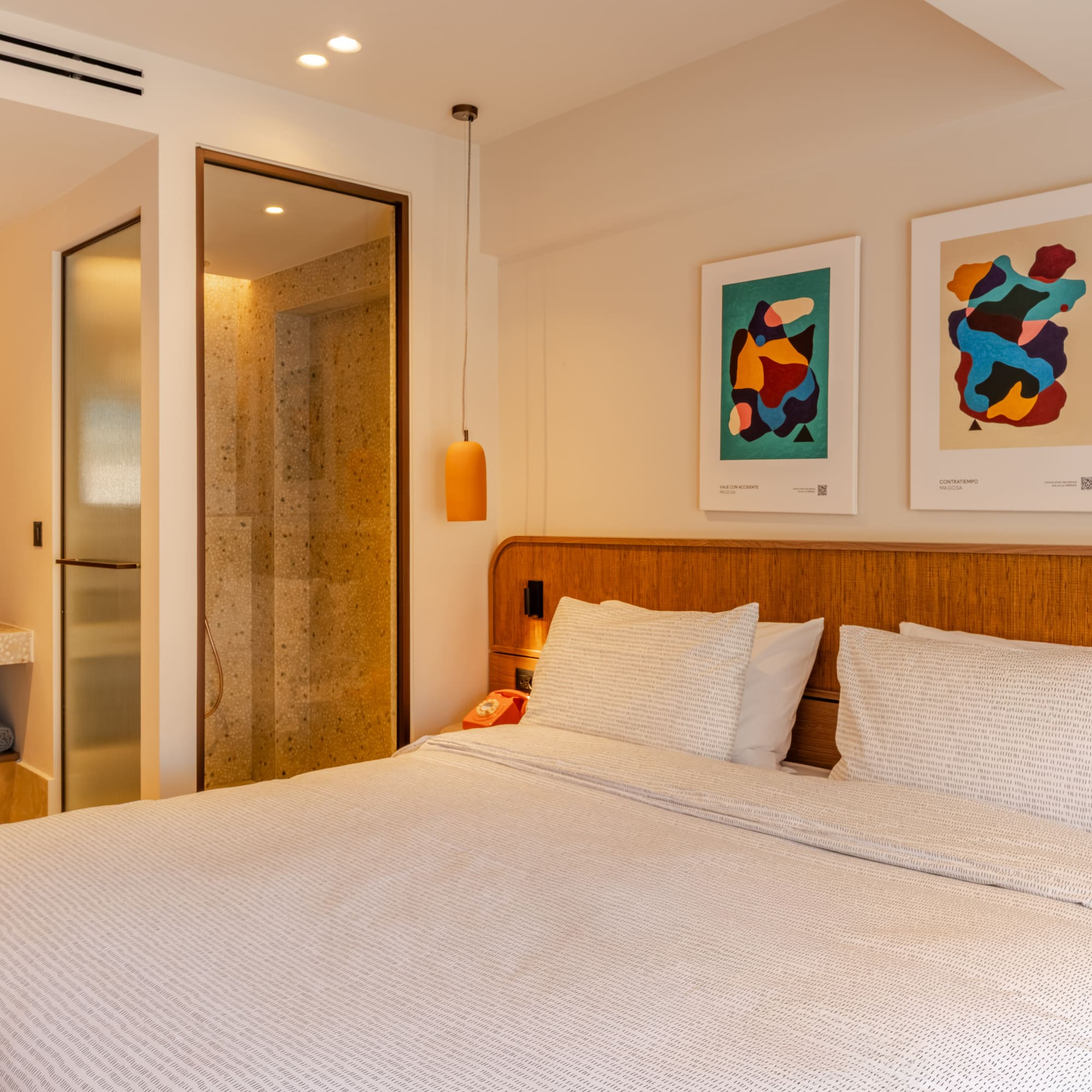 a bed with white sheets and pillows in a room with art on the wall