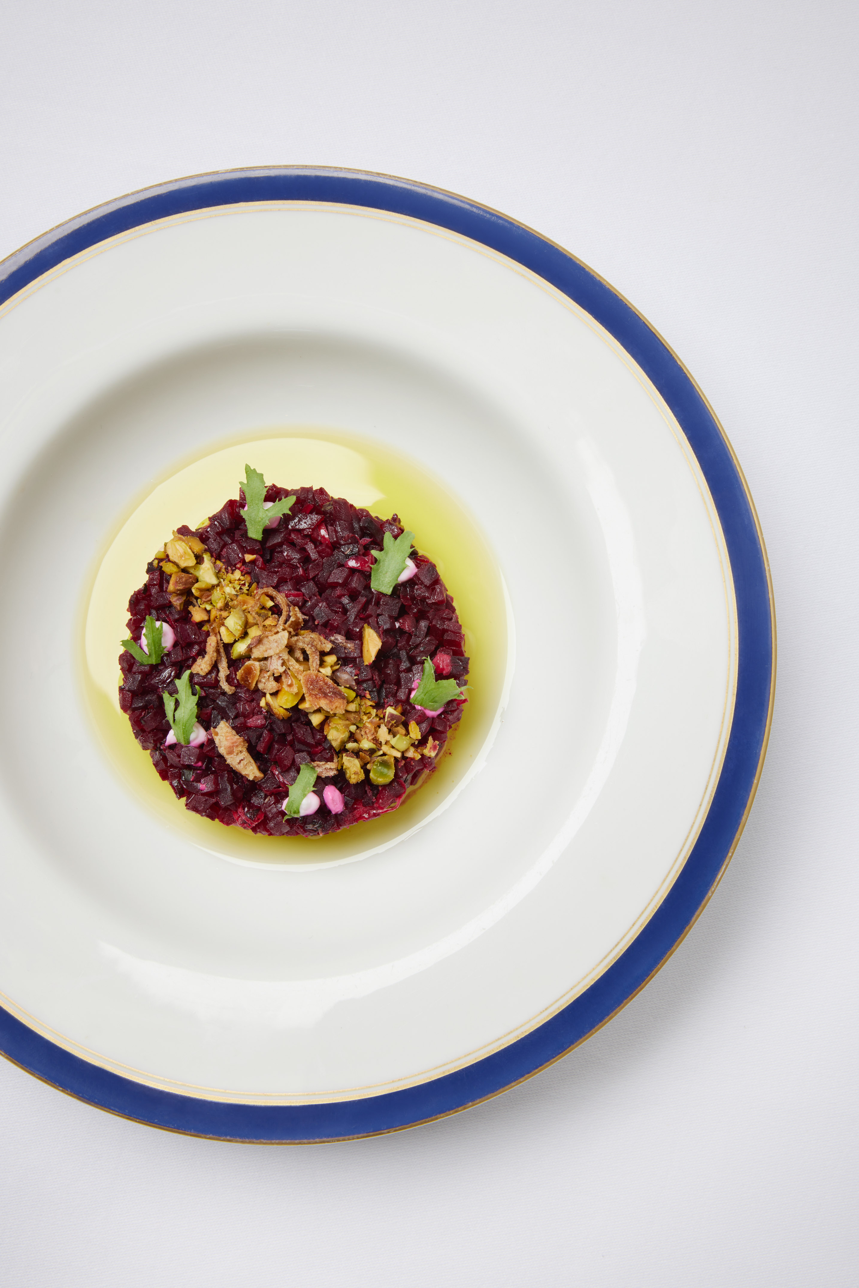 Beetroot tartare with pistachios, crispy shallots, and herbs on a white plate.