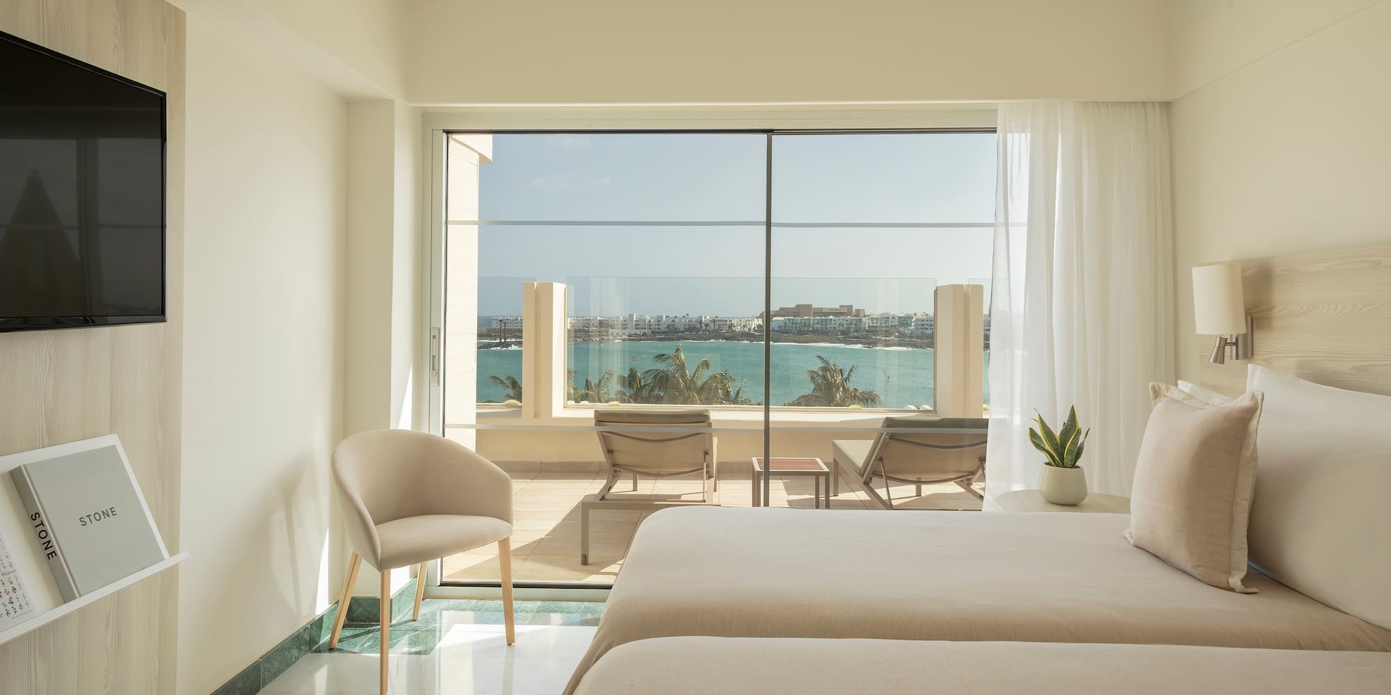 a room with two beds and chairs and a view of the ocean