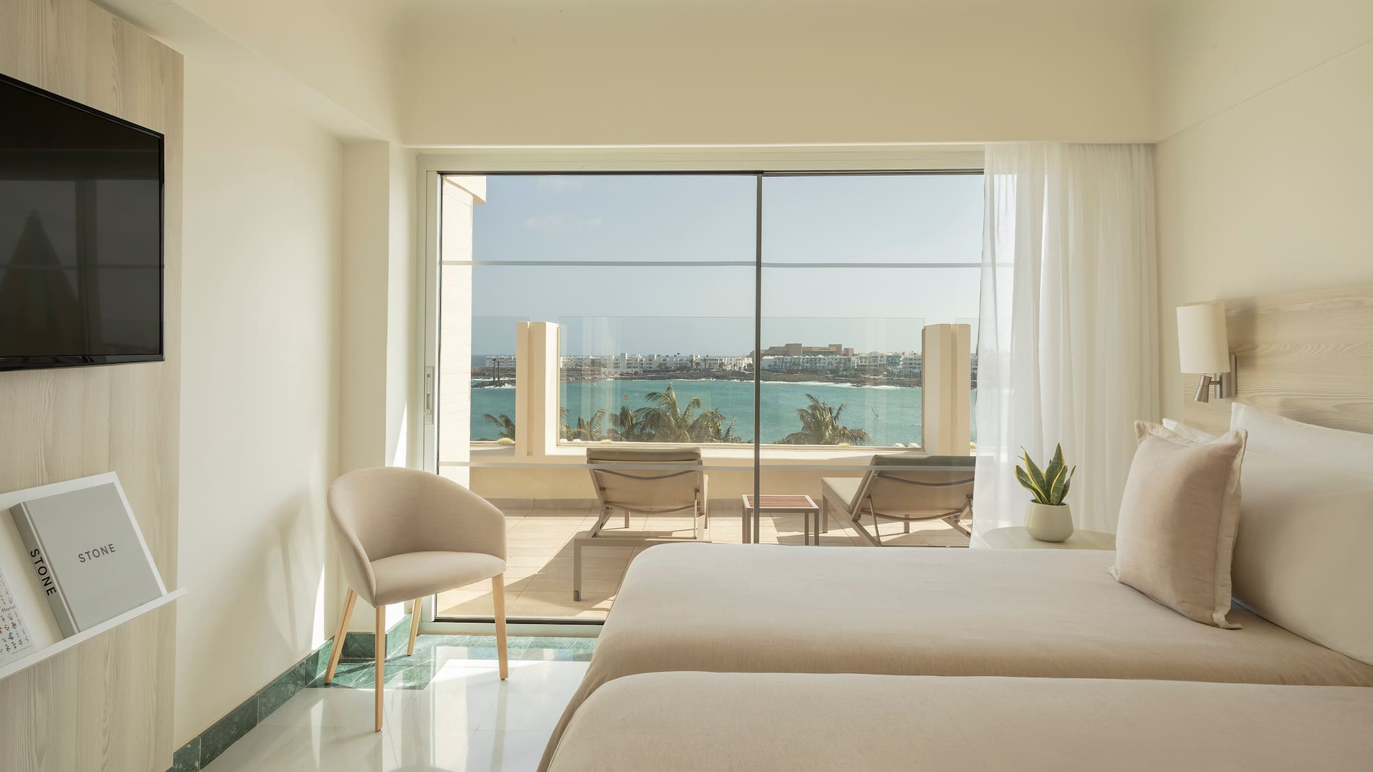 a room with two beds and chairs and a view of the ocean