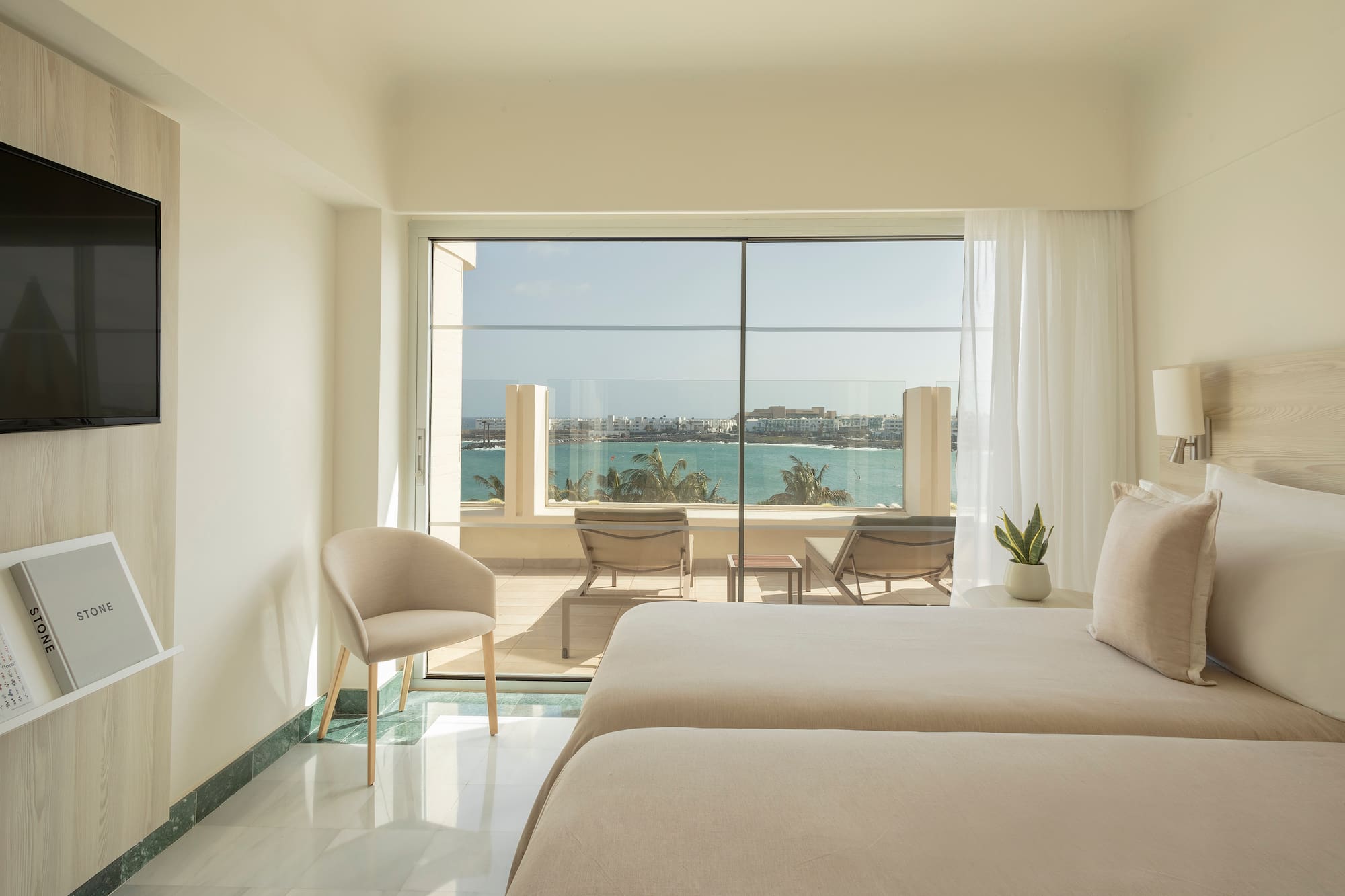 a room with two beds and chairs and a view of the ocean