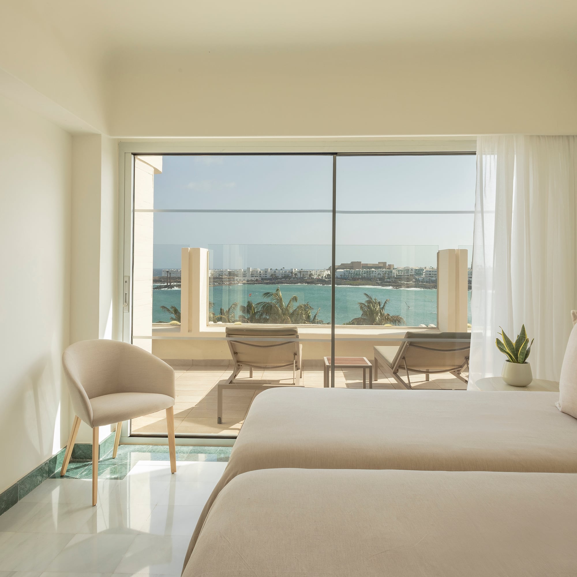 a room with two beds and chairs and a view of the ocean