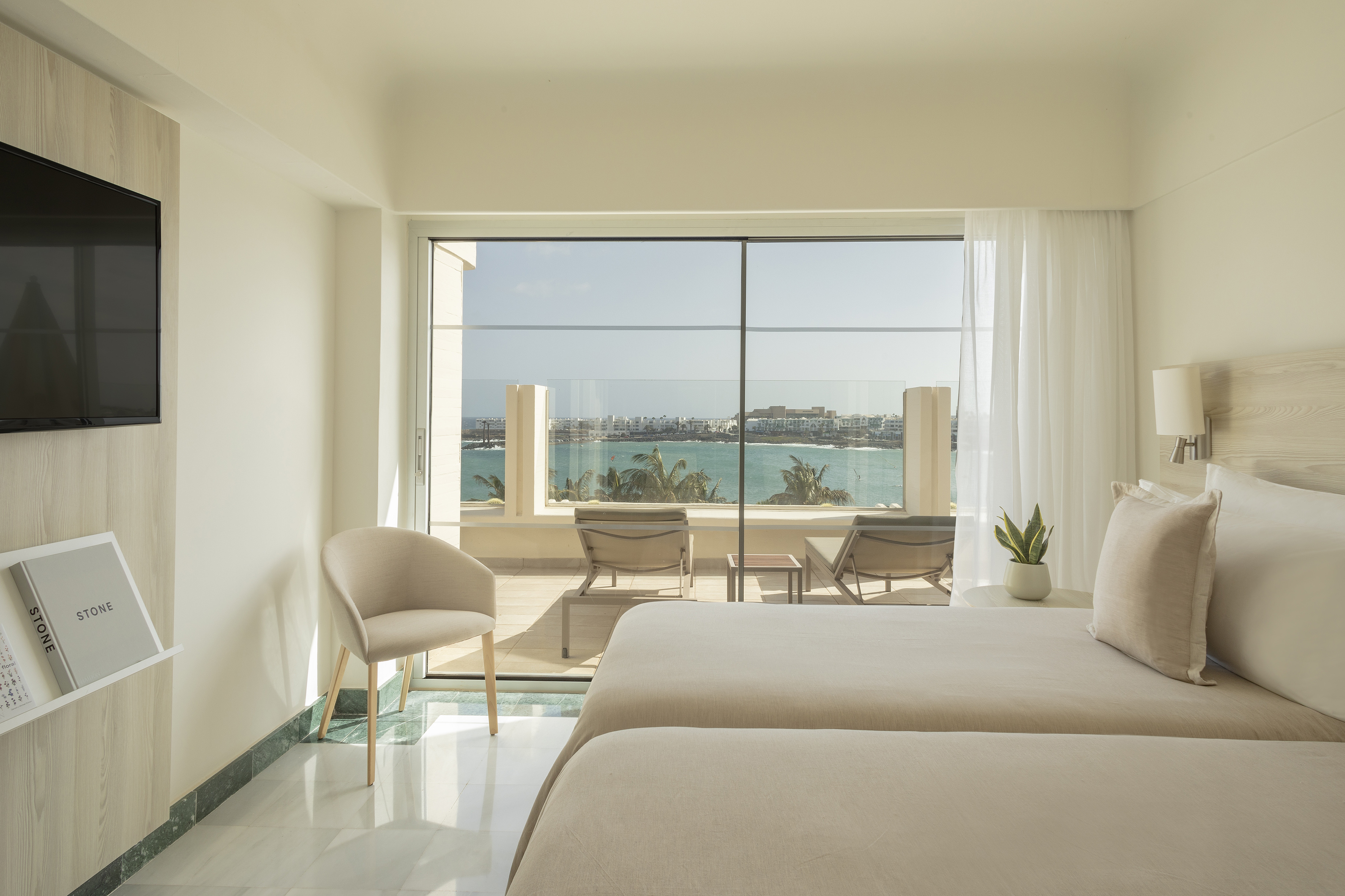 Bright modern hotel room with twin beds, balcony, and panoramic ocean view.