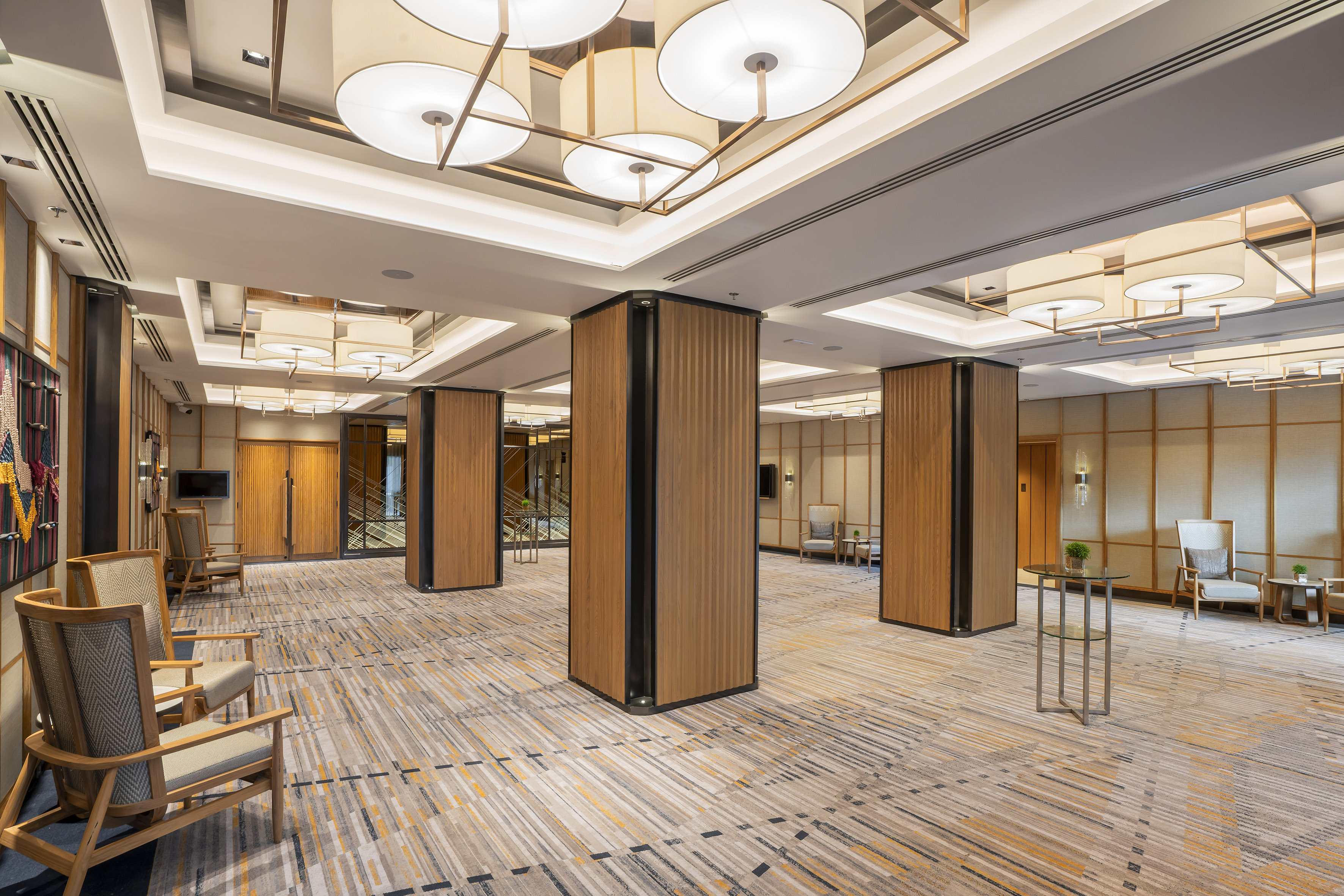 Elegant hotel lobby with modern ceiling lights, wood pillars, and patterned carpet.