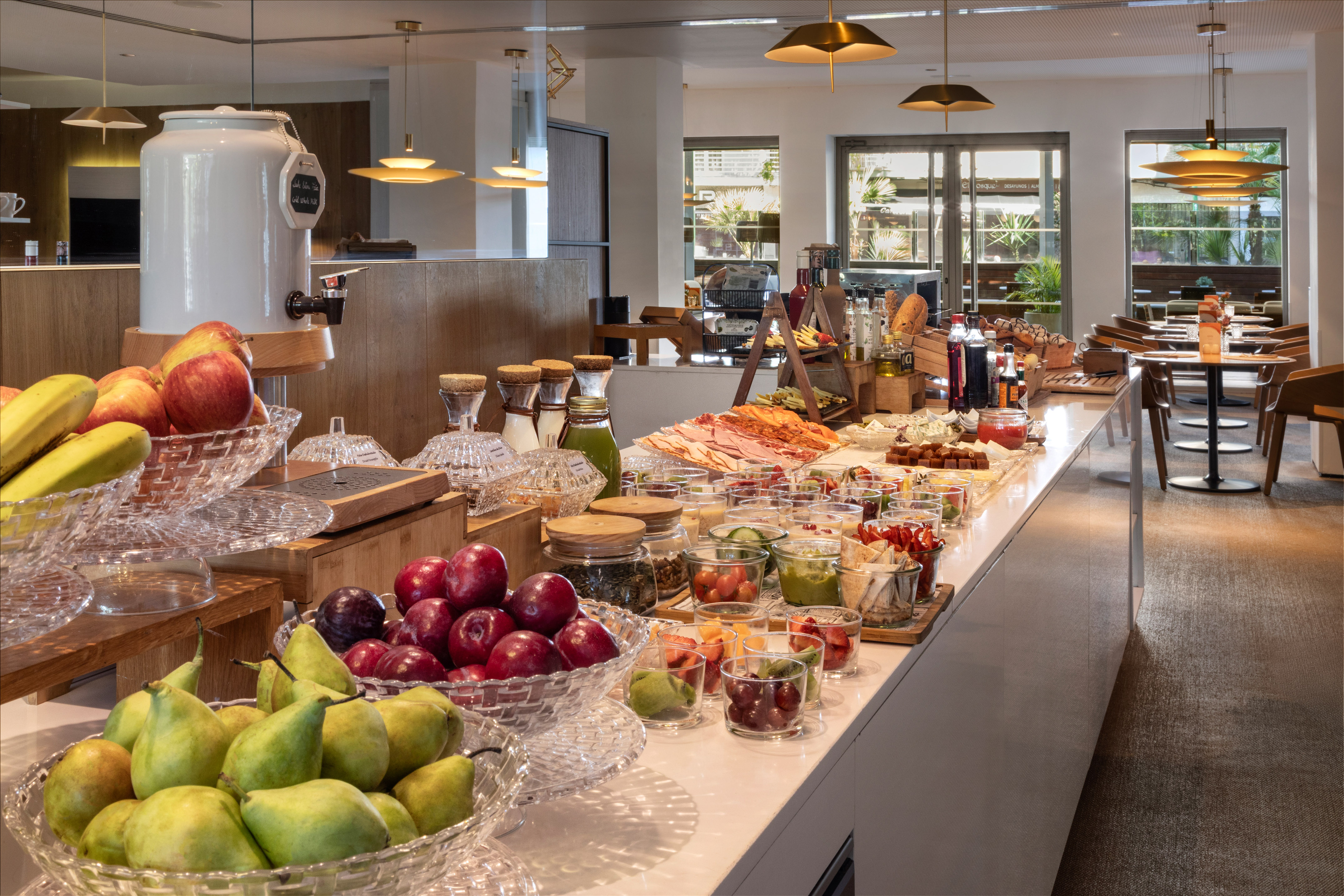 Hotel breakfast buffet with fresh fruit, cold cuts, juices, and modern restaurant.
