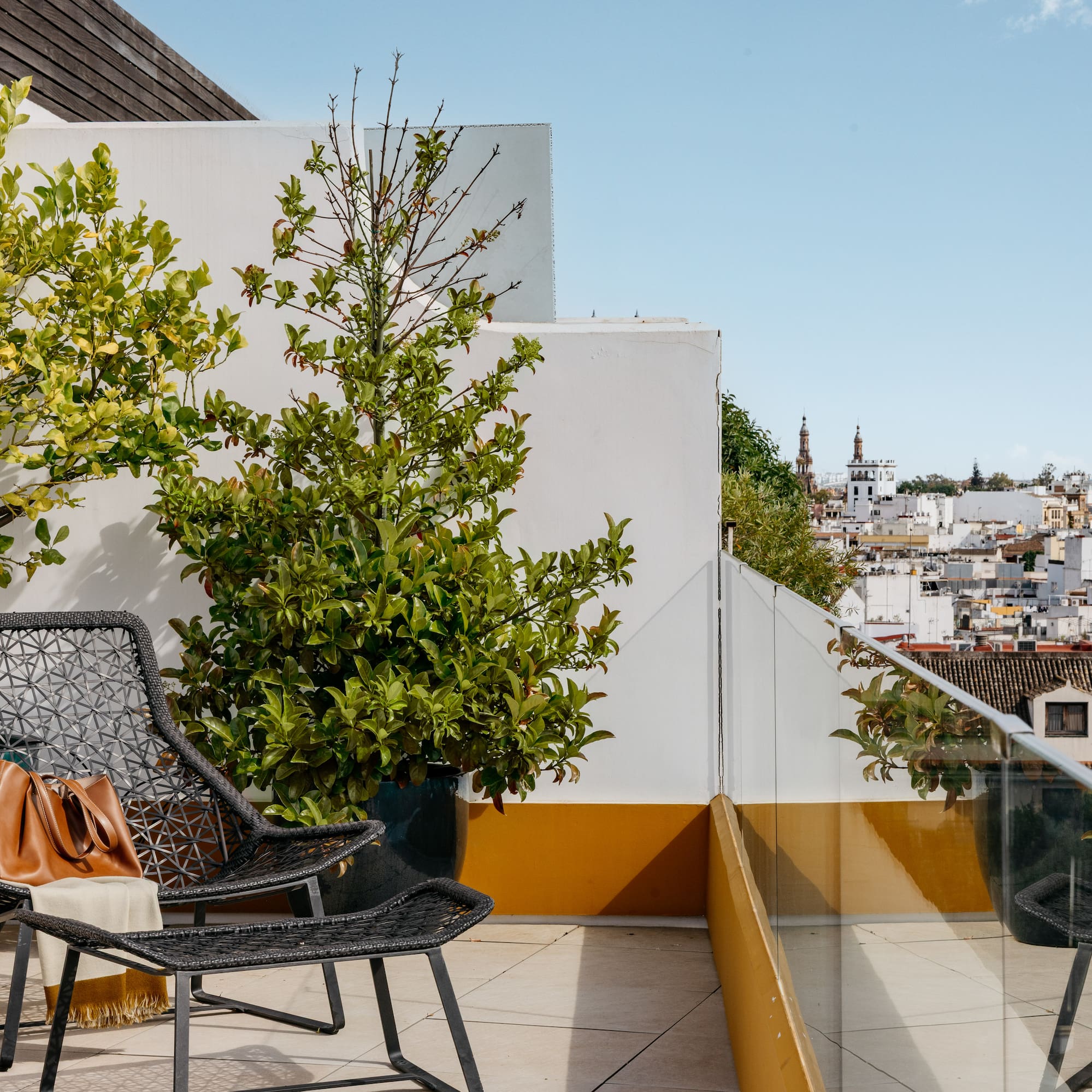 Terraza azotea con sillas, plantas y vista urbana mediterránea.