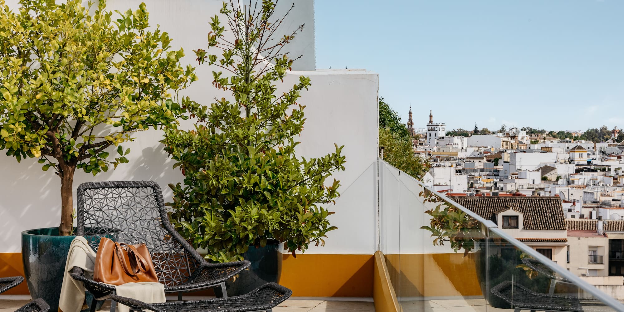 Terraza azotea con sillas, plantas y vista urbana mediterránea.