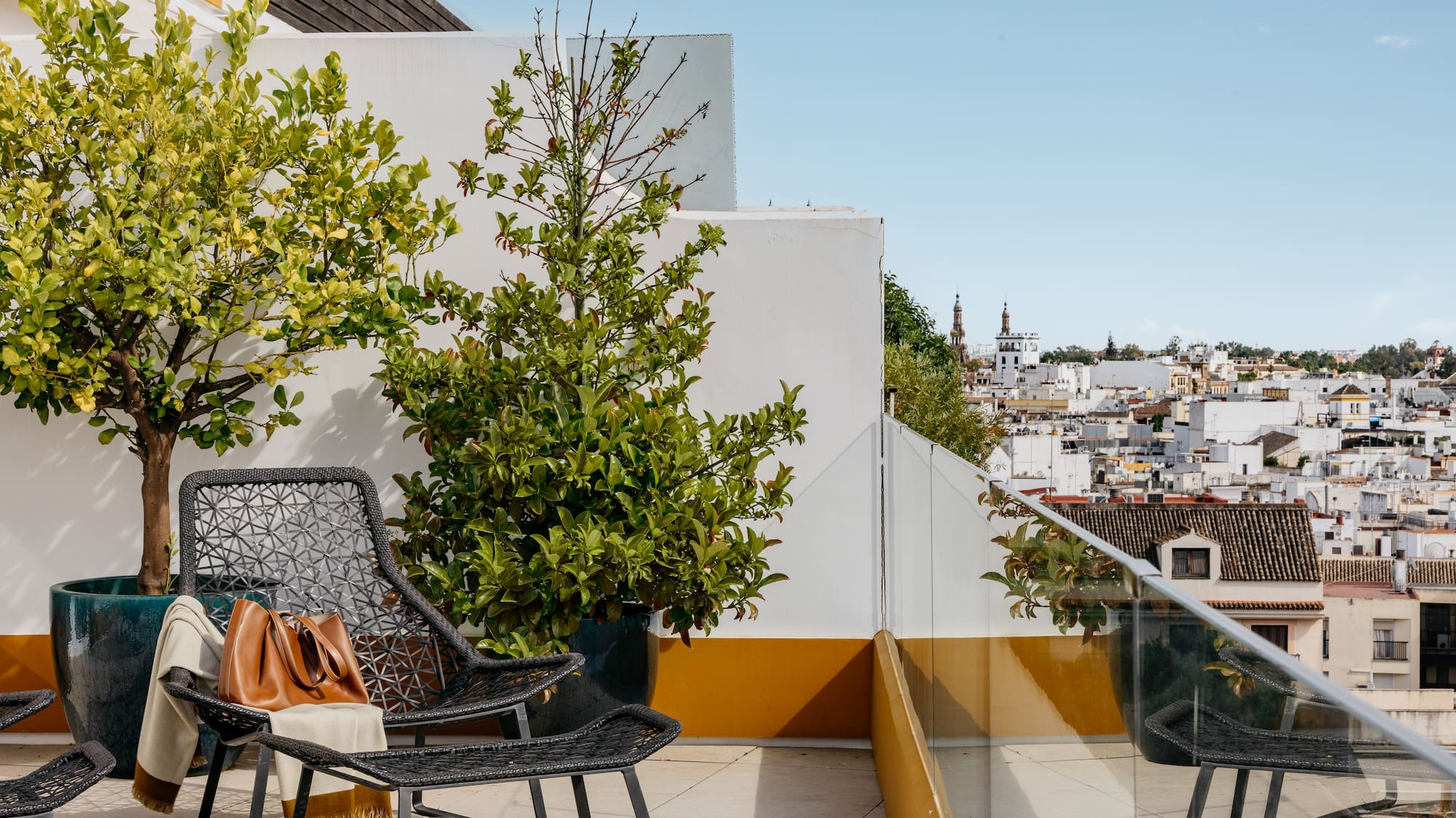 Terraza azotea con sillas, plantas y vista urbana mediterránea.